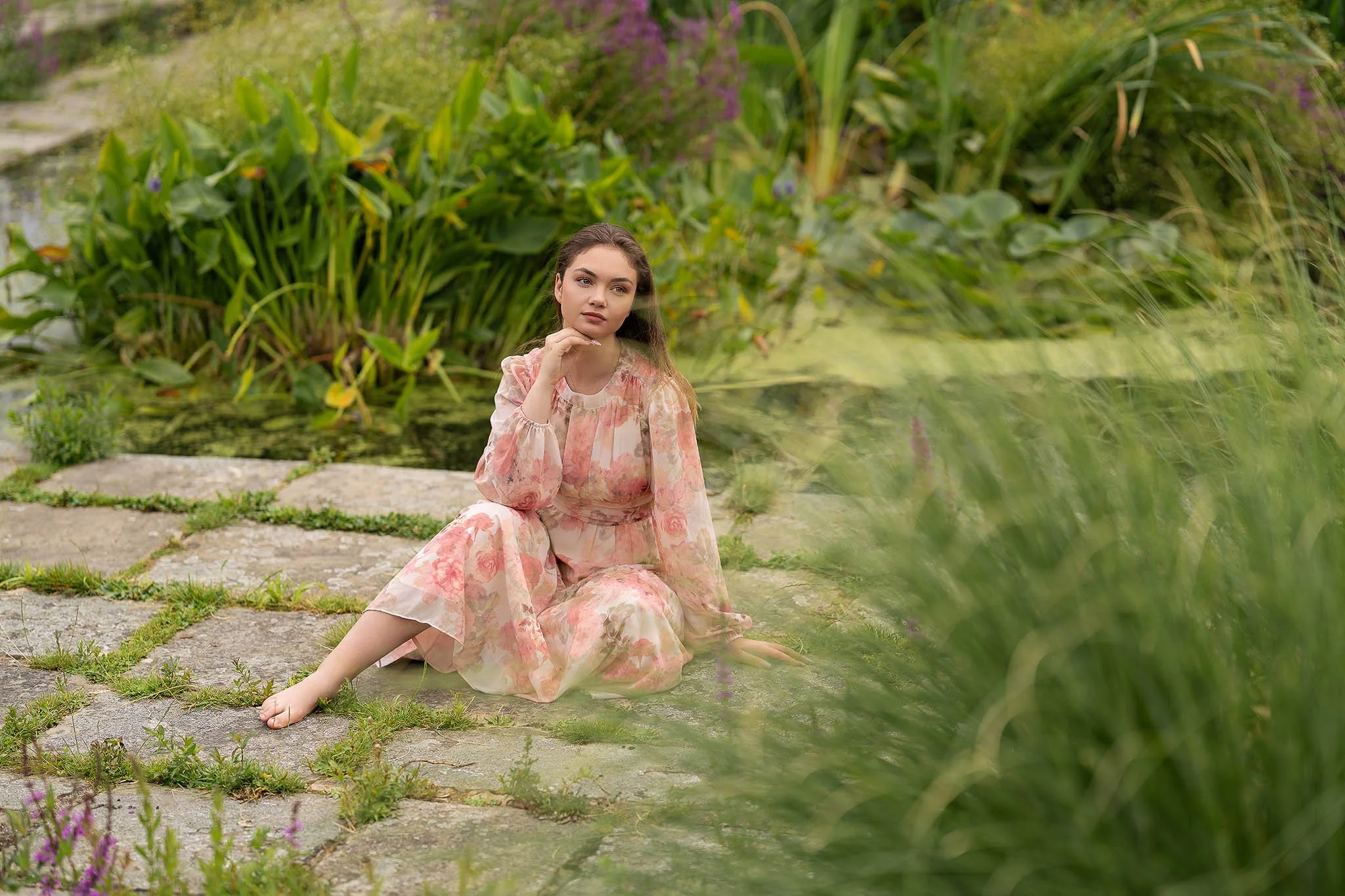 A serene outdoor portrait session in Canons Park, featuring a woman in a soft pink floral dress surrounded by greenery and lily-covered water. A perfect example of Elberta Pictures’ natural, elegant photography style for outdoor minis.