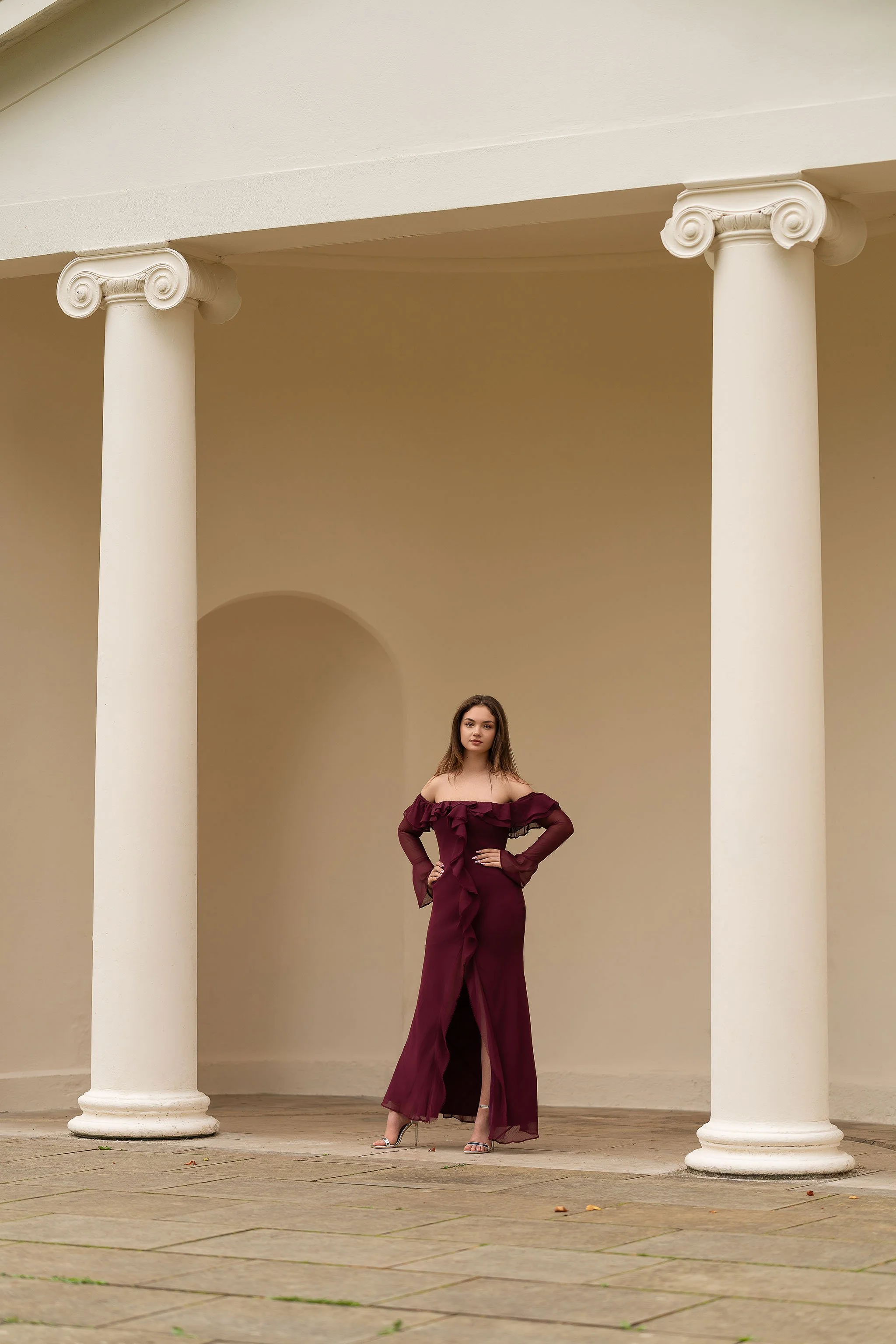 Elegant outdoor portrait of a woman in a burgundy dress framed by classical white columns—minimalist, refined, and timelessly graceful.