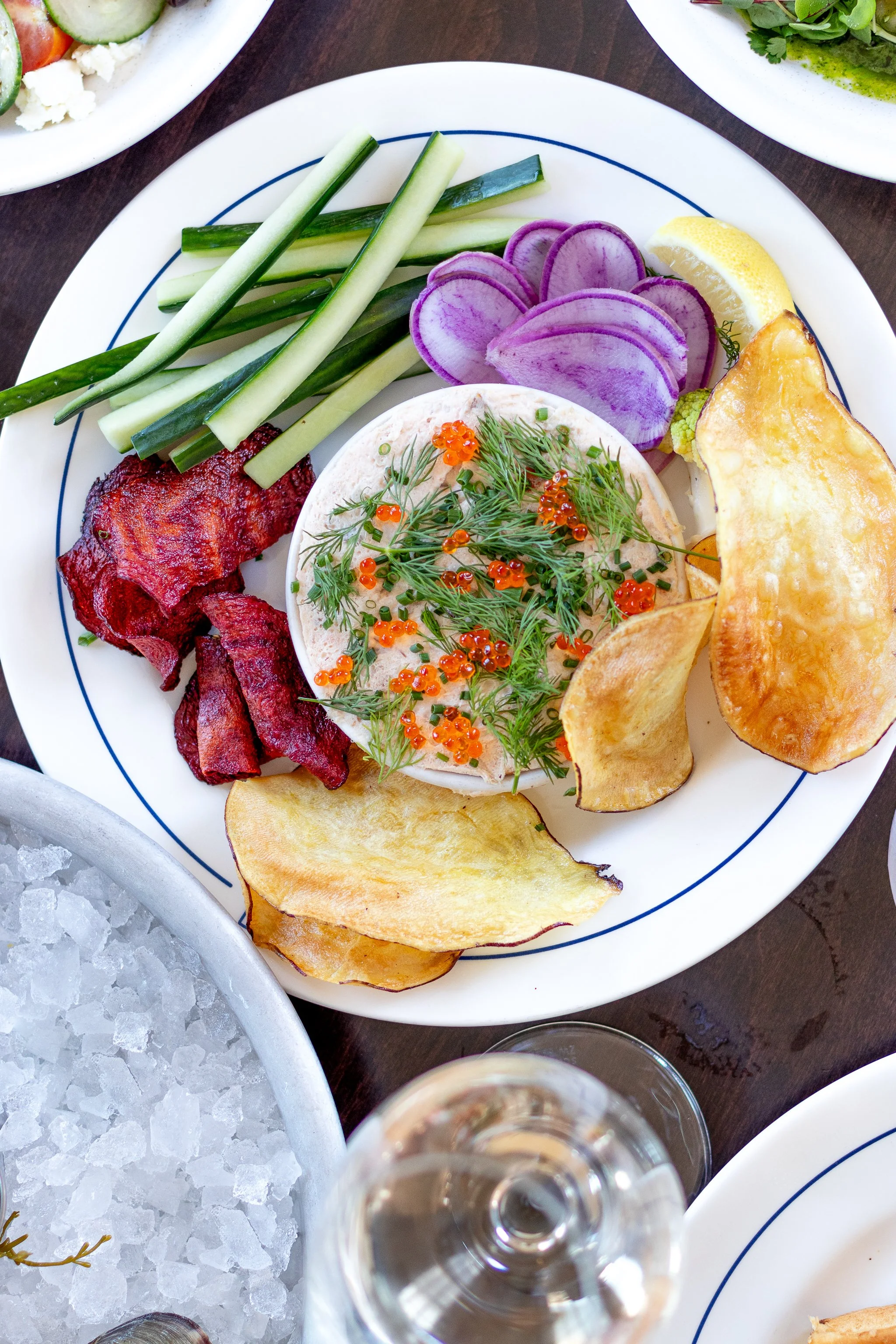 A plate with cucumber sticks, purple radish slices, grilled potato chips, sliced lemon, smoked salmon with herbs and orange roe, and crispy bacon.