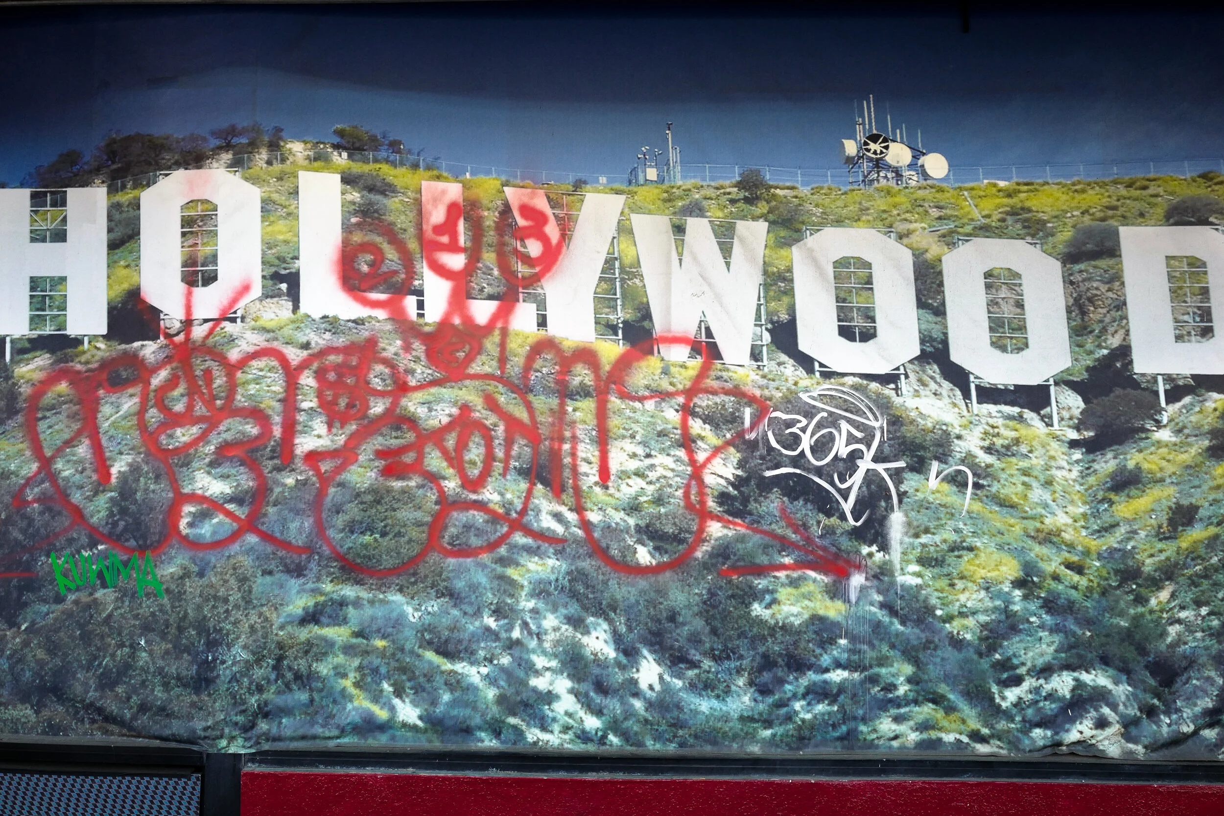 Graffiti-covered Hollywood sign on a hillside, with various tags and spray paint in red, white, and green over the sign.