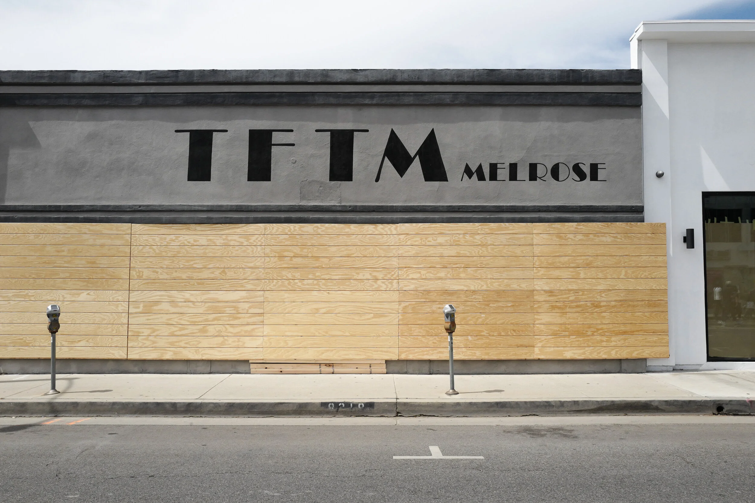Exterior of a building with the sign 'TFTM Melrose' on the upper wall, featuring a combination of black lettering on a gray background and light wood paneling below.