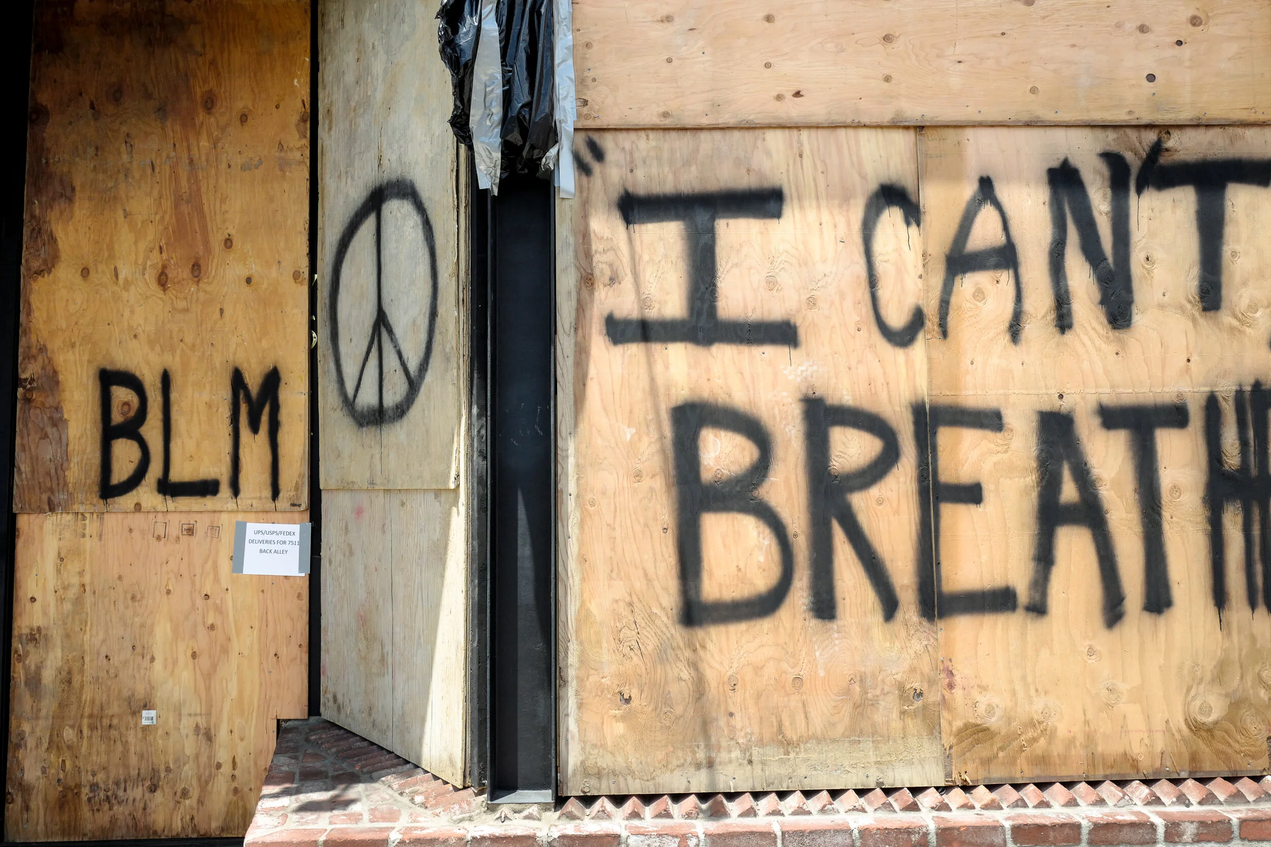 Plywood boards with spray-painted messages: 'BLM' with a peace sign symbol, and 'I CAN'T BREATH'.