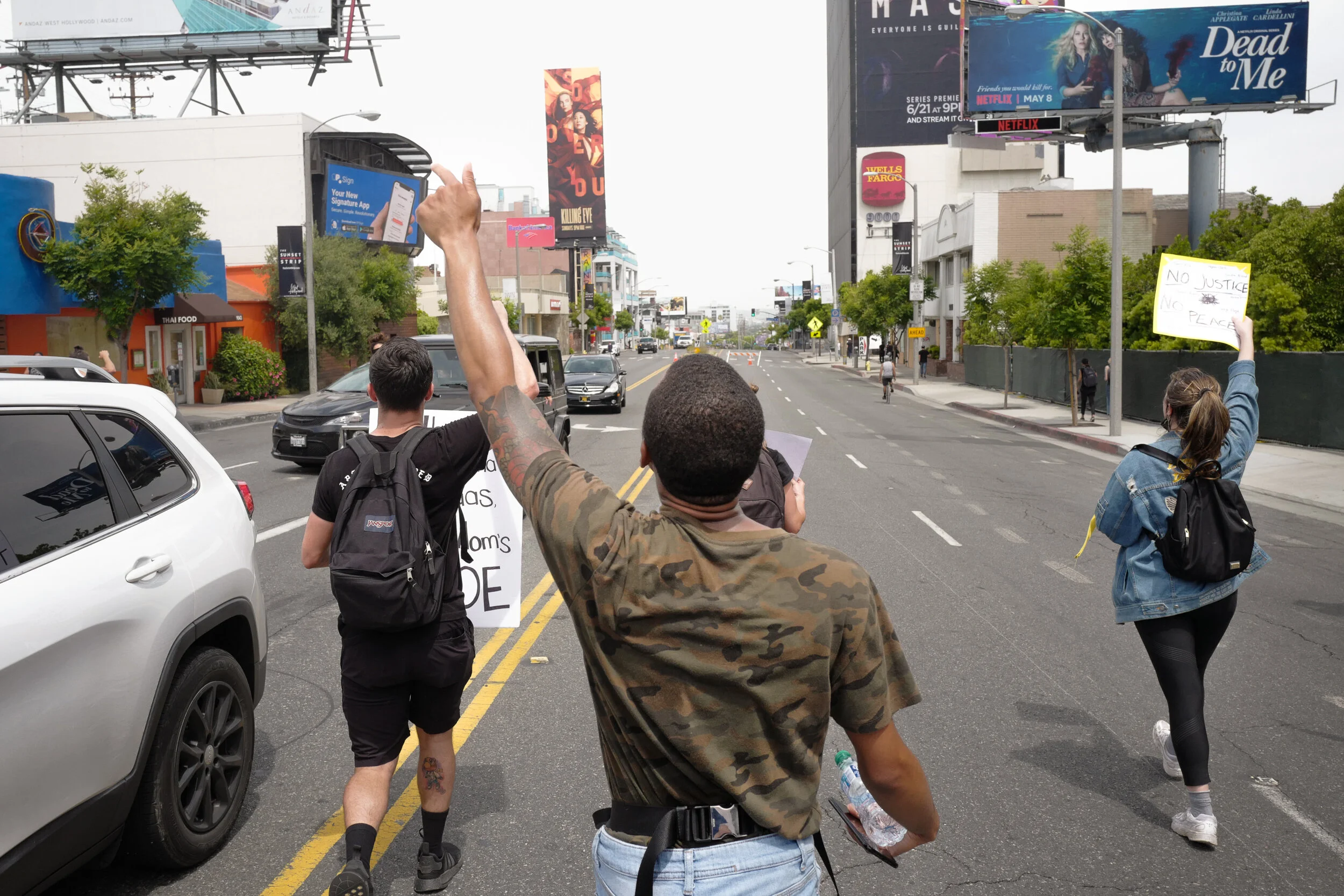 Protesters walking on a city street holding signs with messages such as 'No Justice No Peace' and others.