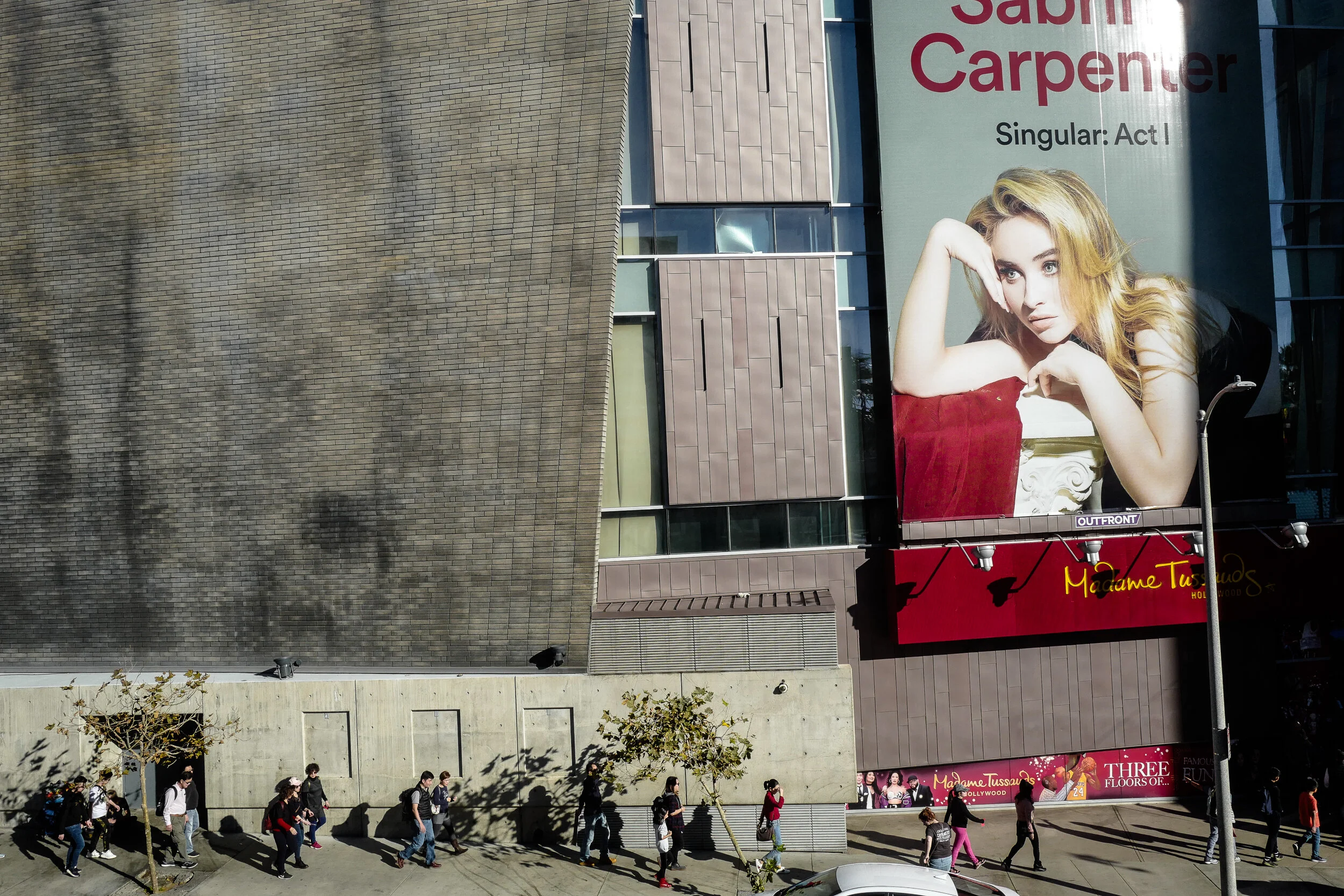 Large billboard advertising a woman with red hair for Shakespeare's 'Romeo and Juliet' at Madame Tussauds in Hollywood, California, with pedestrians walking on the sidewalk below.