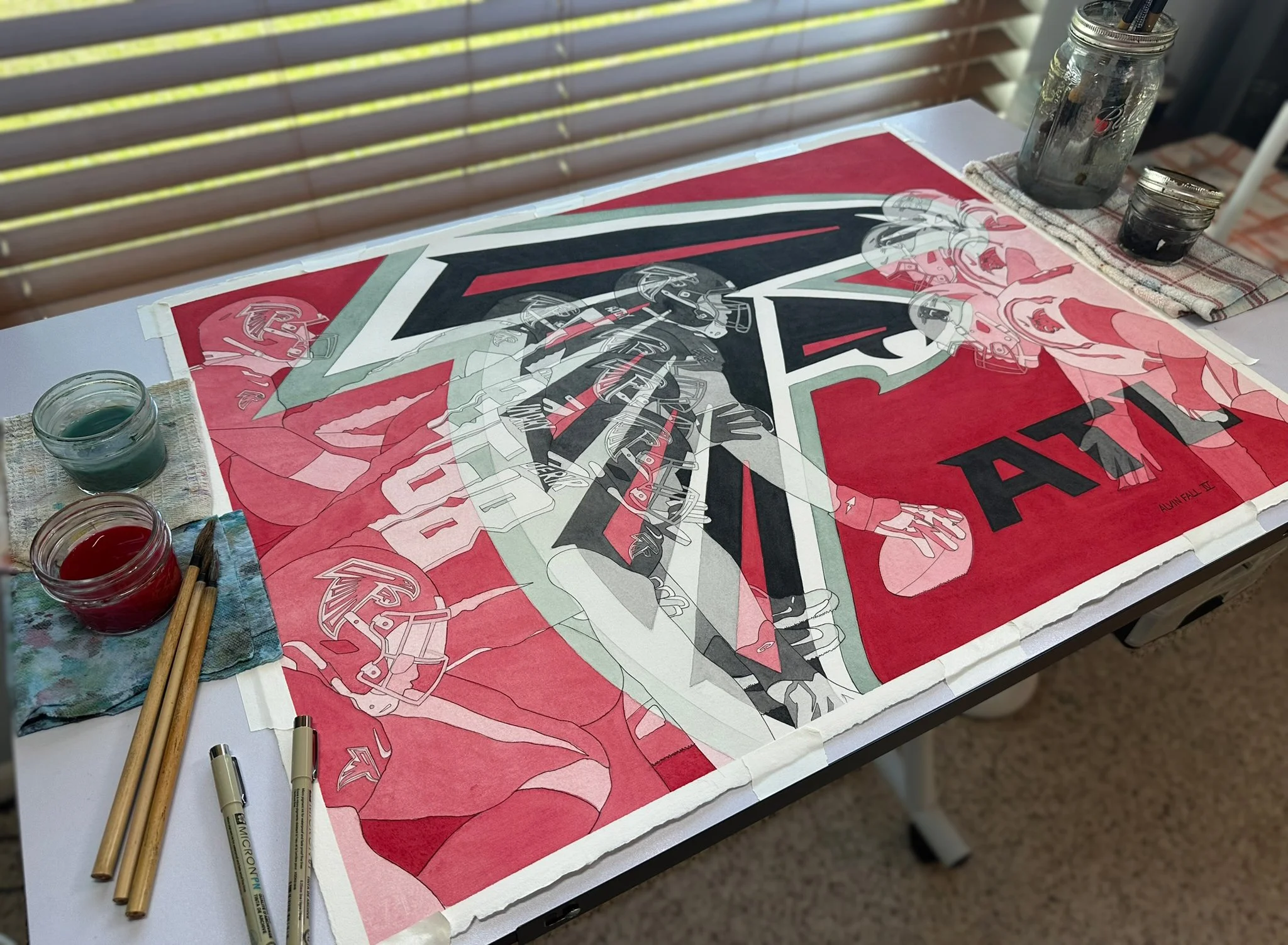 The completed Falcons watercolor on the art desk with watercolor jars and brushes, showing the dynamic composition where transparent players emerge through the angular falcon emblem