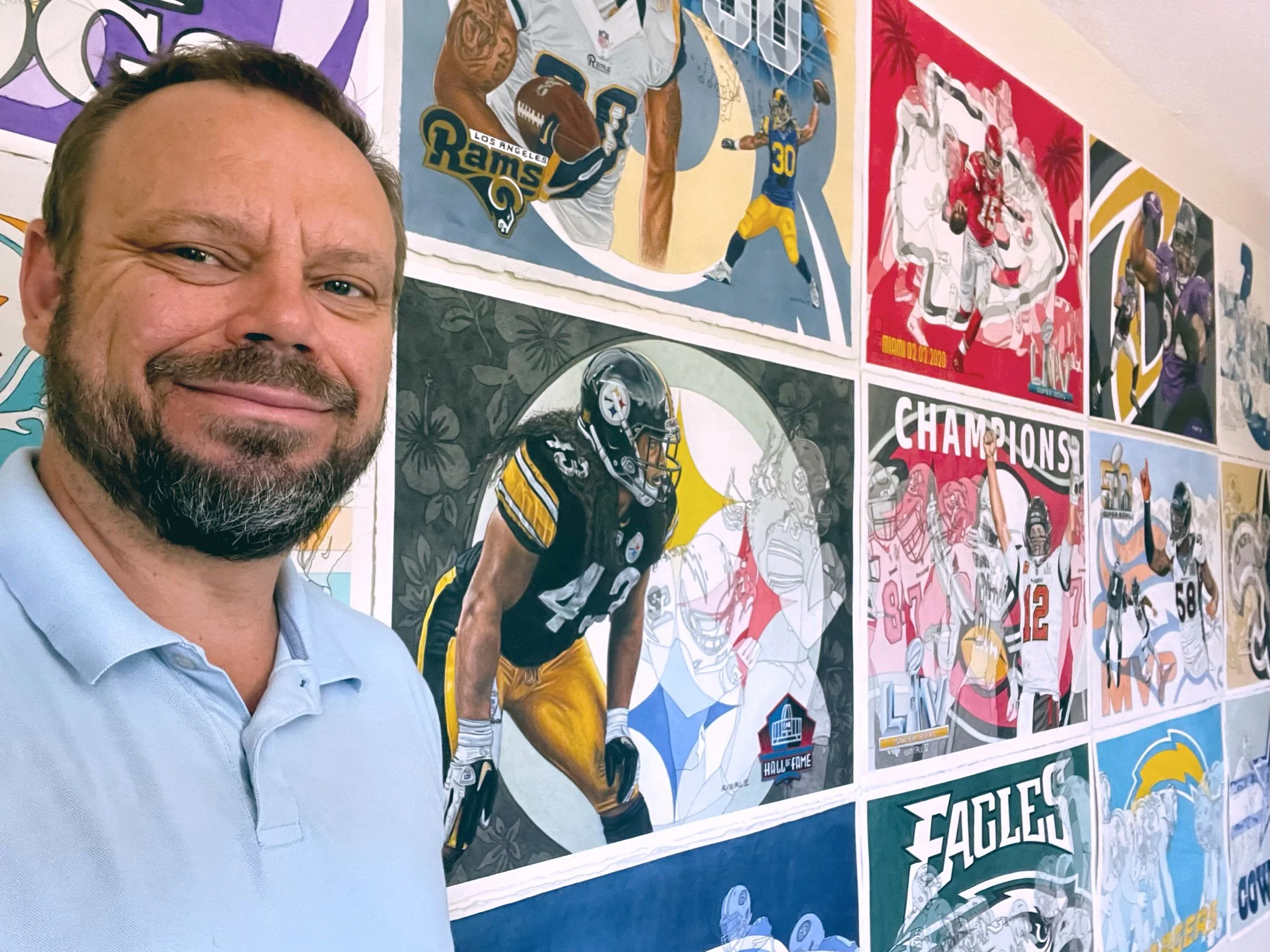 Photograph of Artist Alvin Fall standing in front of a wall of his artwork at Alvin Fall Studio