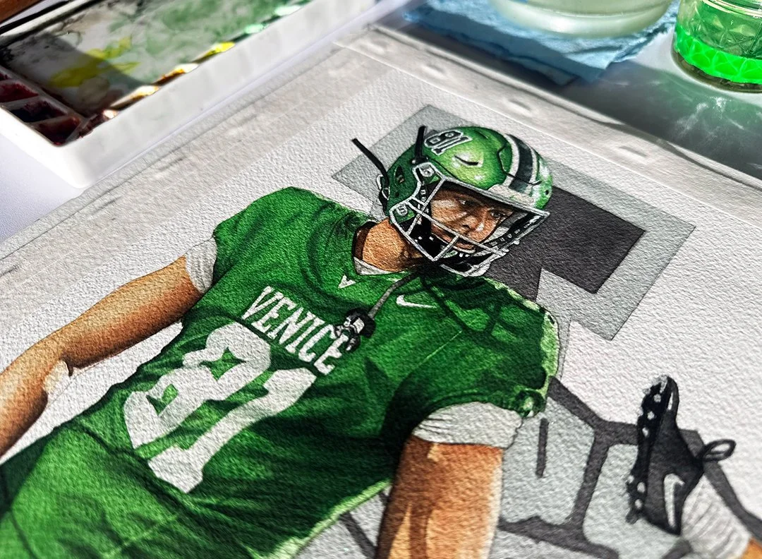 A desk-level view of the finished painting showing the rich texture of Arches cold press watercolor paper and the layered detail work on Reynolds' face and jersey.