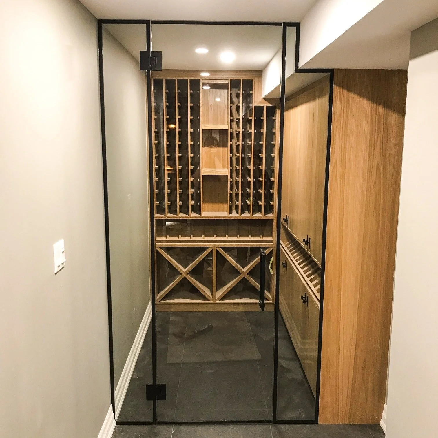Modern wine cellar with glass door, featuring wooden wine racks, storage compartments, and wine bottle holders.