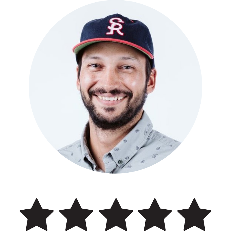 Portrait of a smiling man wearing a baseball cap with a logo, gray patterned button-up shirt, against a white background.