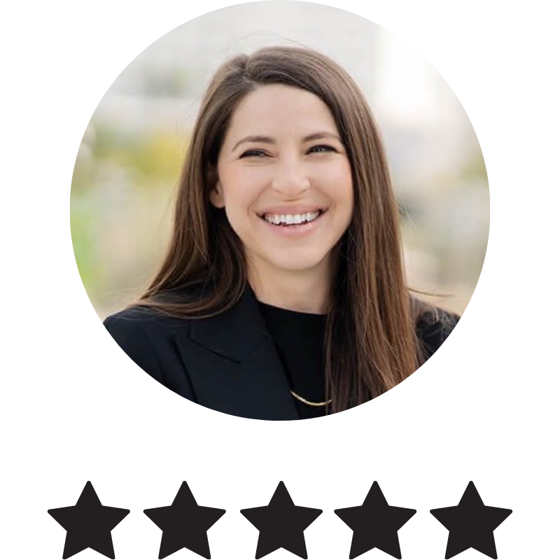 A woman with long brown hair smiling outdoors in a professional black blazer.