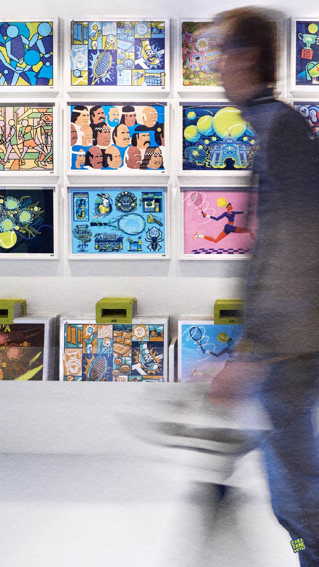 A person walking past an art gallery wall featuring colorful illustrations and paintings, with a row of green boxes below the artwork.