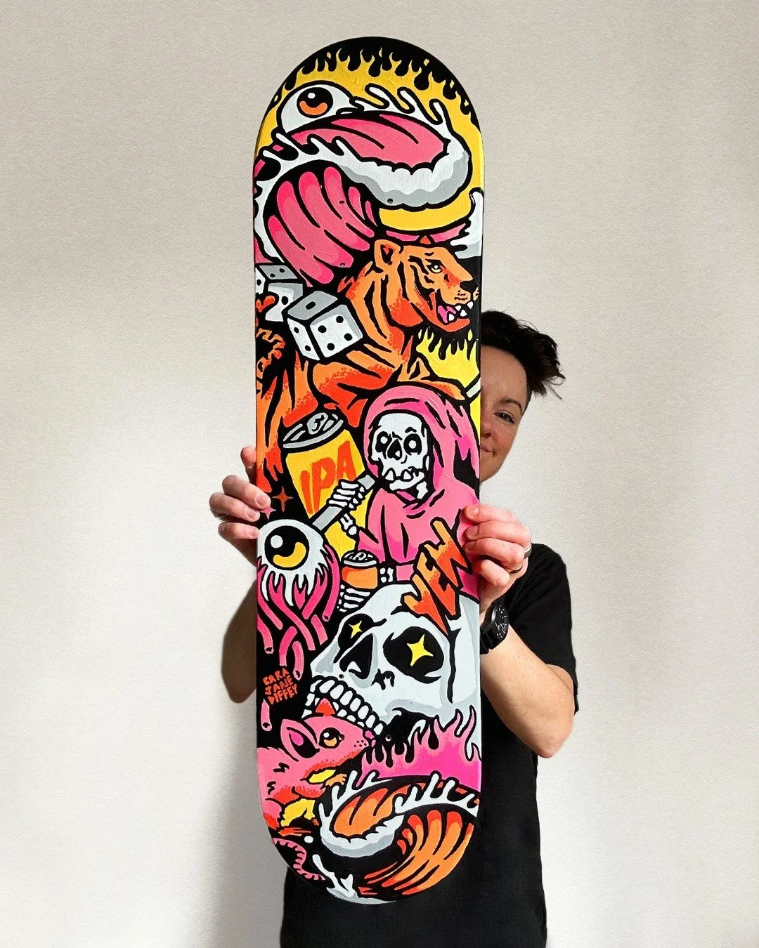 Person holding a skateboard with colorful street art-style illustrations including a flaming eye, lion, skeleton, skull, and various abstract designs.