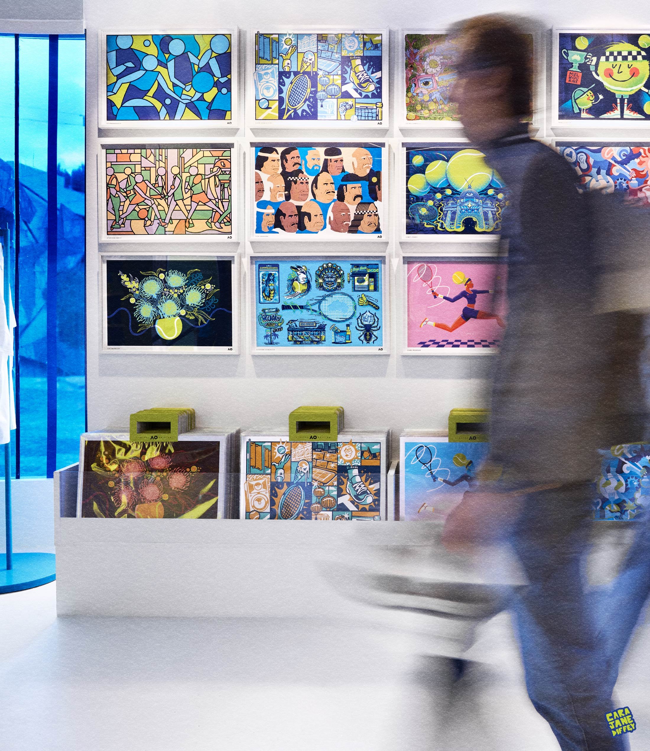 An art gallery with colorful, abstract prints on the wall. A person walking past a display table with more artwork. The gallery has a modern, minimalistic design.