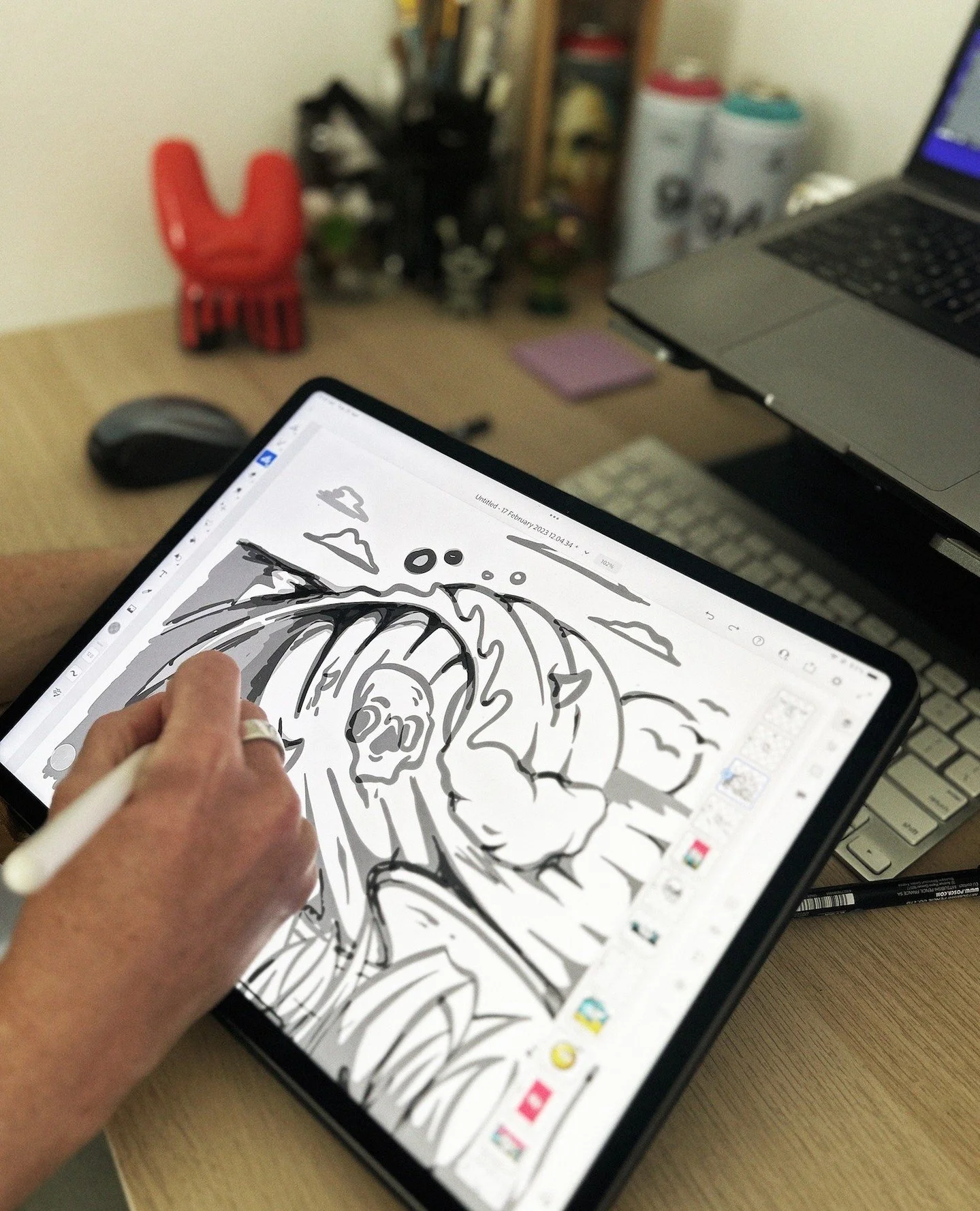 A person sketching a black and white fantasy character with horns on a digital tablet, with a desk and computer in the background.