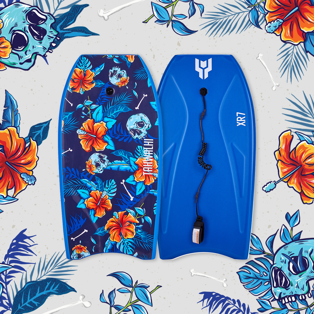 Two wakeboards on a tropical-themed background with orange hibiscus flowers, blue foliage, and skull designs, one with a colorful skull and floral pattern and the other solid blue with a traction pad.