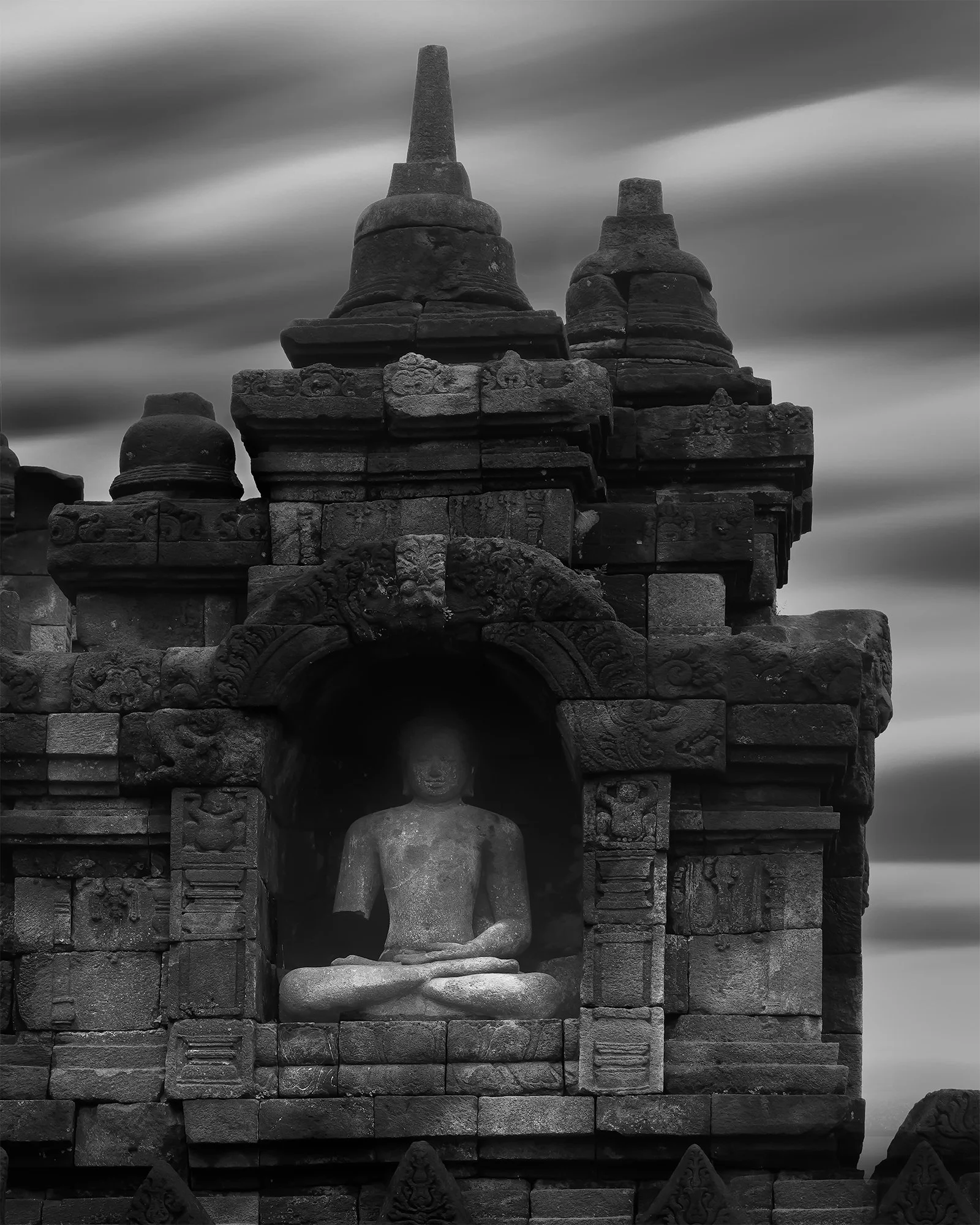 A black and white photograph of an ancient stone temple with a seated Buddha statue inside a small arched shrine.