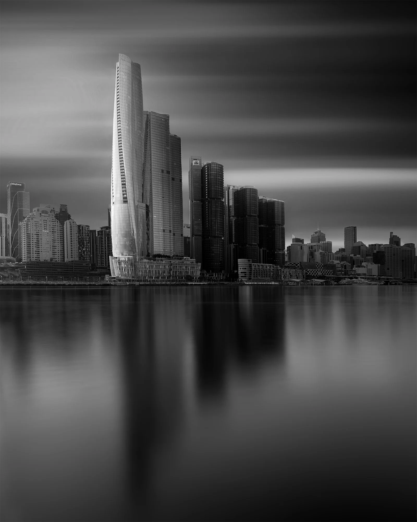Black and white photograph of a modern city skyline reflected in water, with tall skyscrapers including a distinctive curved building.