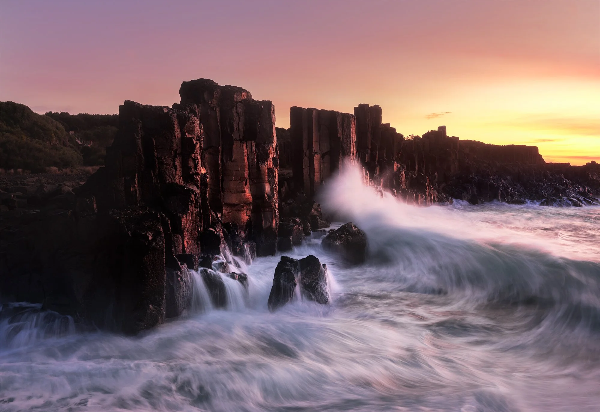 Sunset over rugged cliffside with crashing waves at the ocean during twilight.