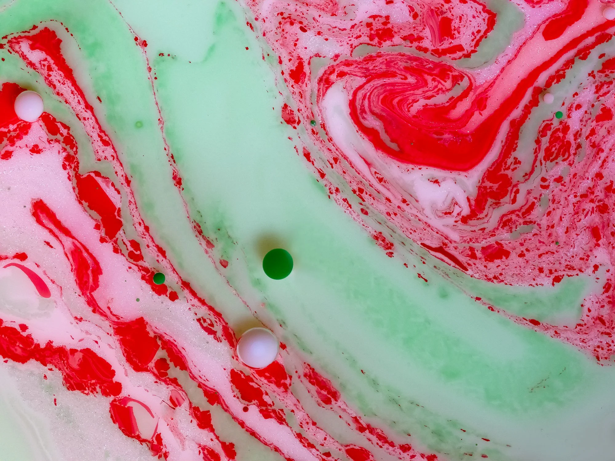 Swirling mixture of red, green, and white liquid with bubbles.