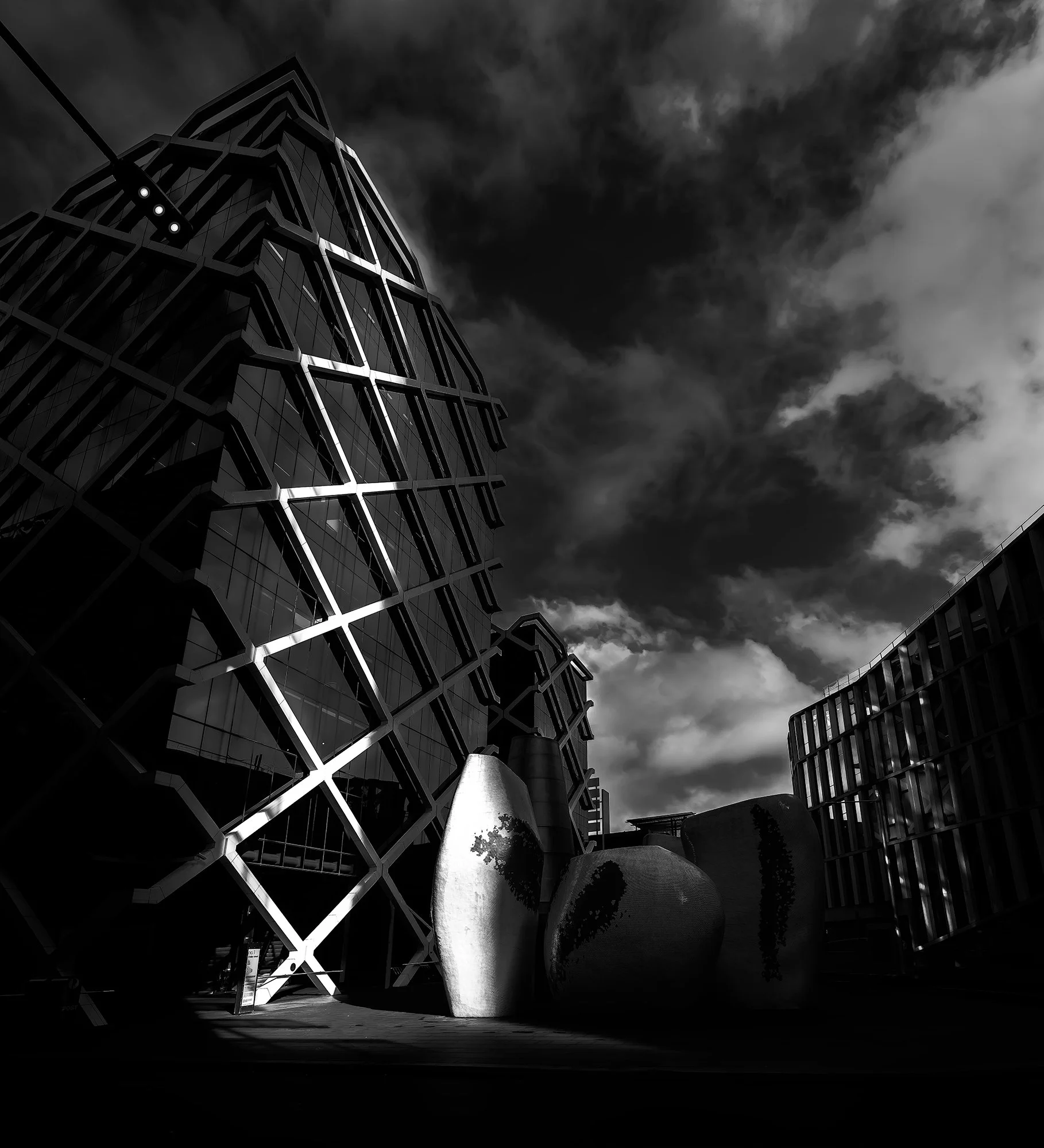Black and white photo of modern glass and steel buildings with large sculptural vases in the foreground, under a cloudy sky.