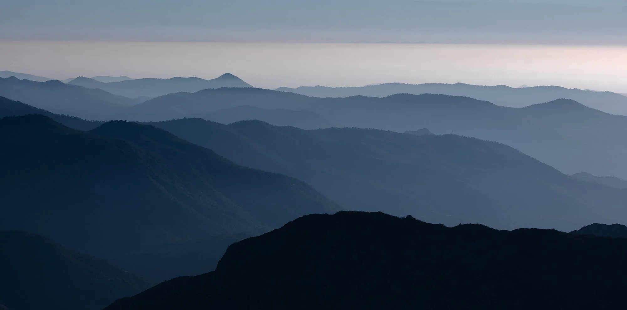 Multiple mountain ridges with a layered view and cloudy sky in the background.