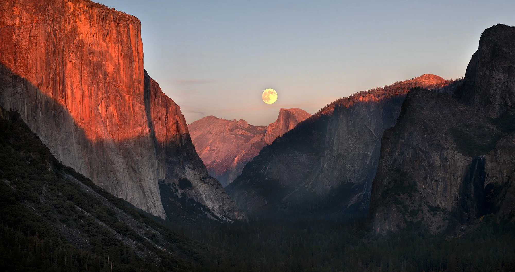 Sunset over a mountain valley with the full moon visible in the sky