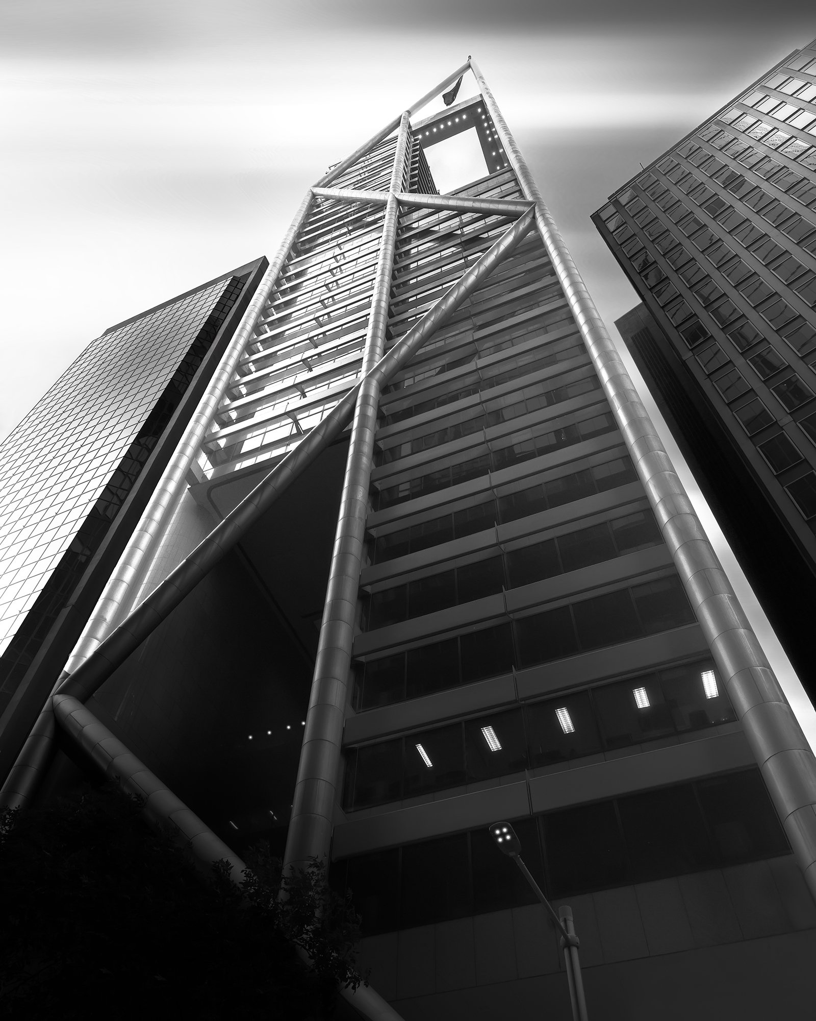 Black and white photo of a tall modern skyscraper with glass windows and a distinctive framework at the top, surrounded by other high-rise buildings.