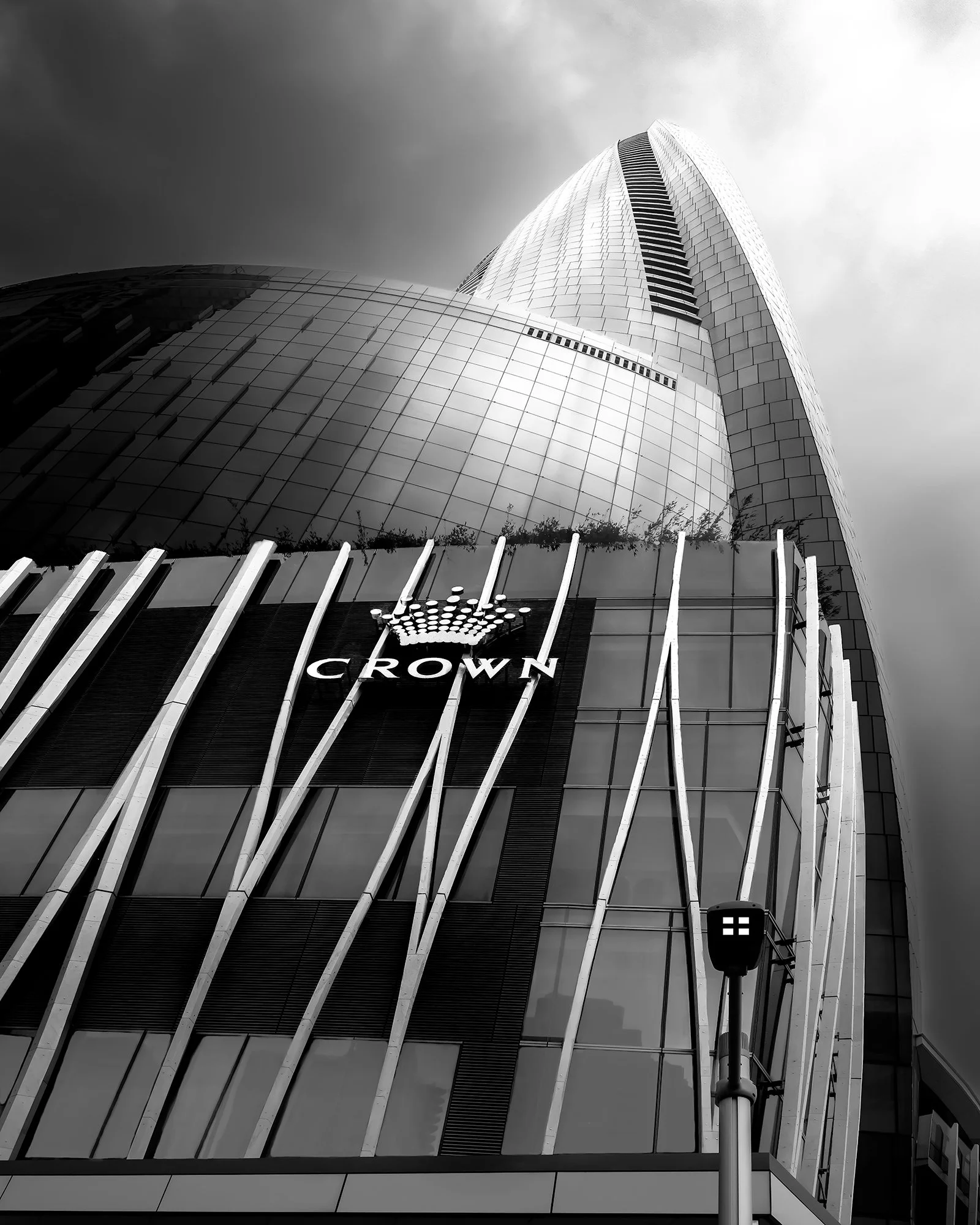 Low-angle view of a modern skyscraper with a sign and crown logo for Crown on the building facade, with a cloudy sky in the background.