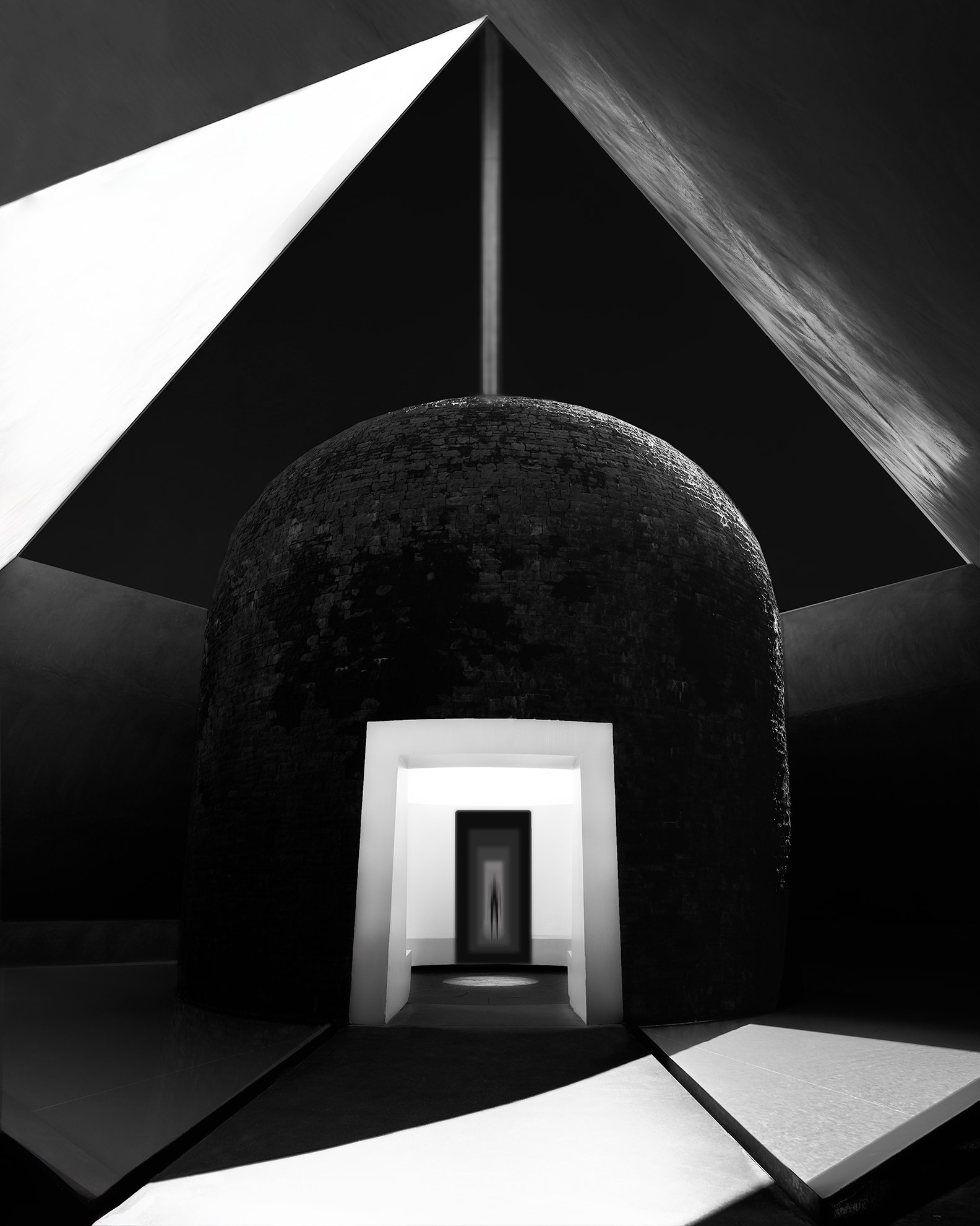 A black and white photograph of an architectural interior featuring a domed brick structure with a centered doorway at the front. Above, geometric shapes and a beam of light form a pyramid or triangular shape.