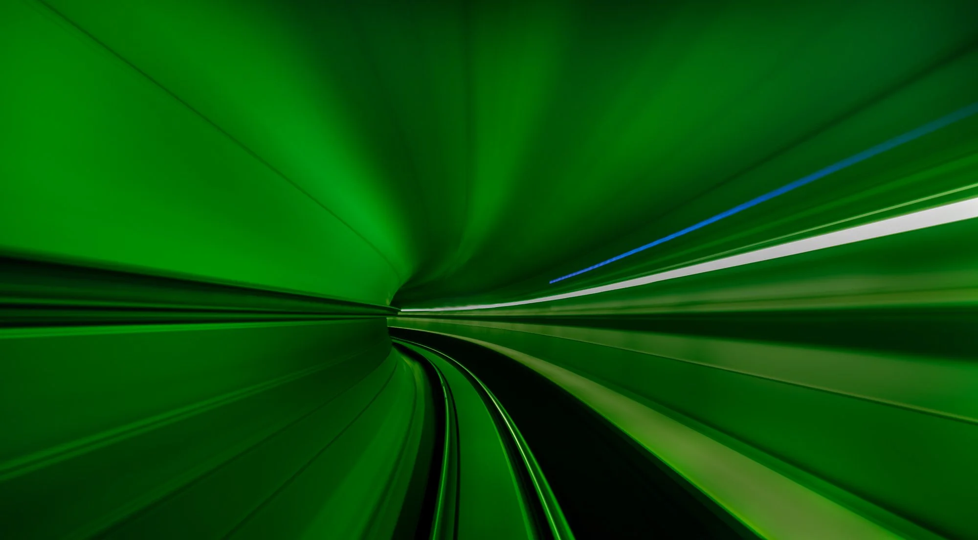 A long, dark tunnel illuminated with green and blue lights, creating a futuristic and dynamic appearance.