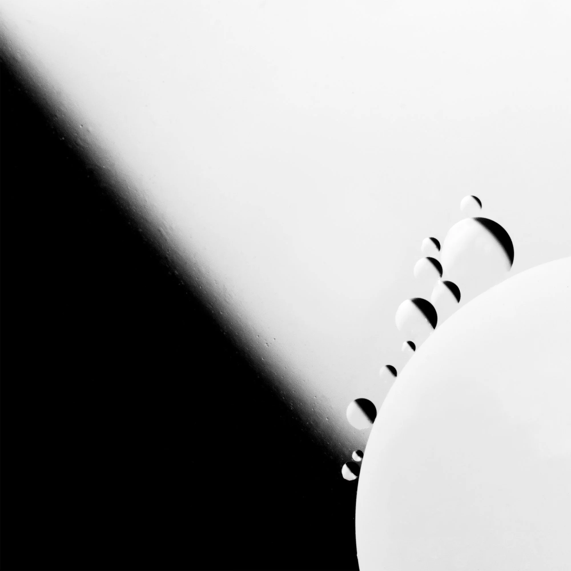 Black and white abstract image of small and large spheres arranged on a curved surface with a gradient background.