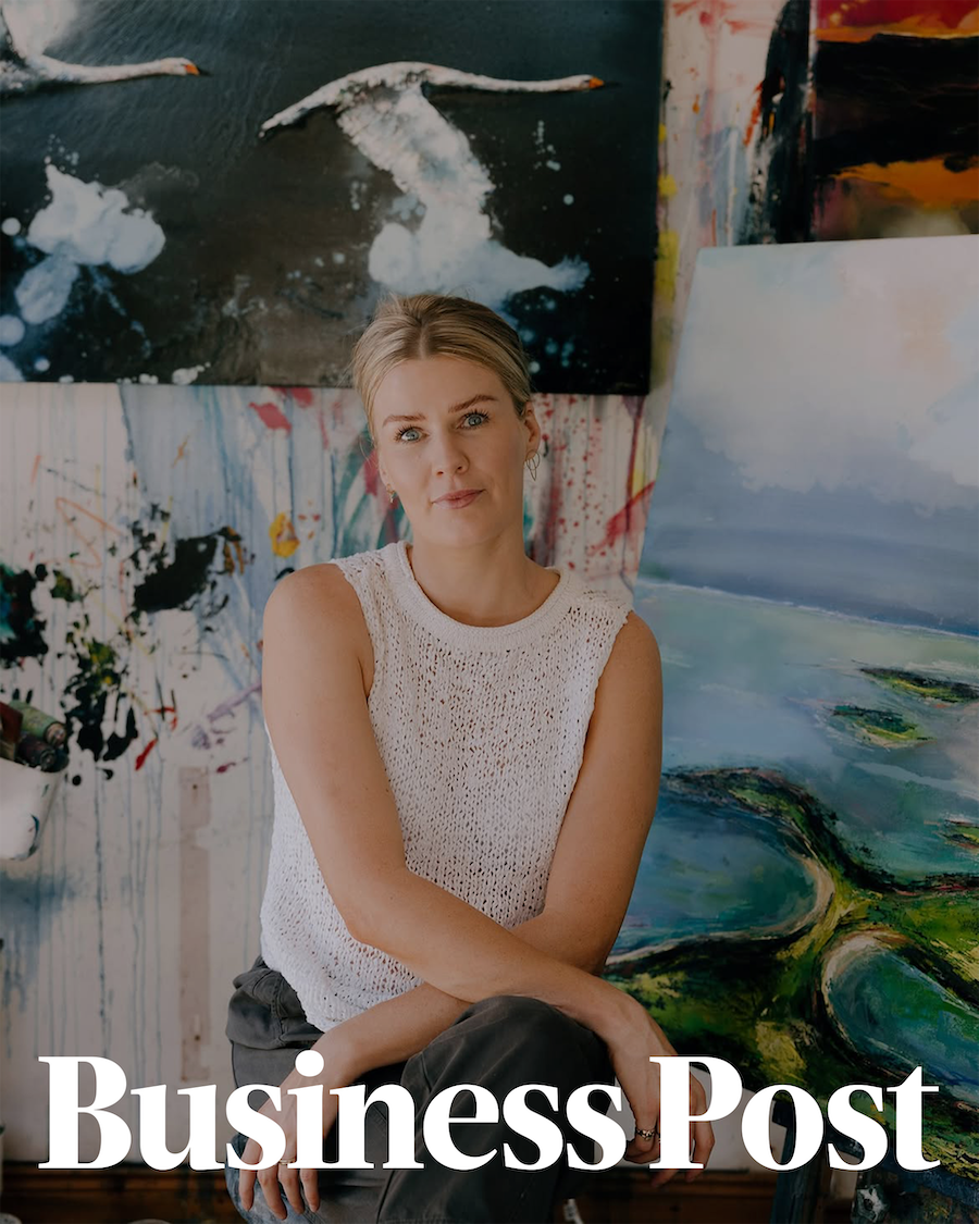Portrait of a woman sitting in an art studio, surrounded by colorful abstract paintings, with a confident expression.