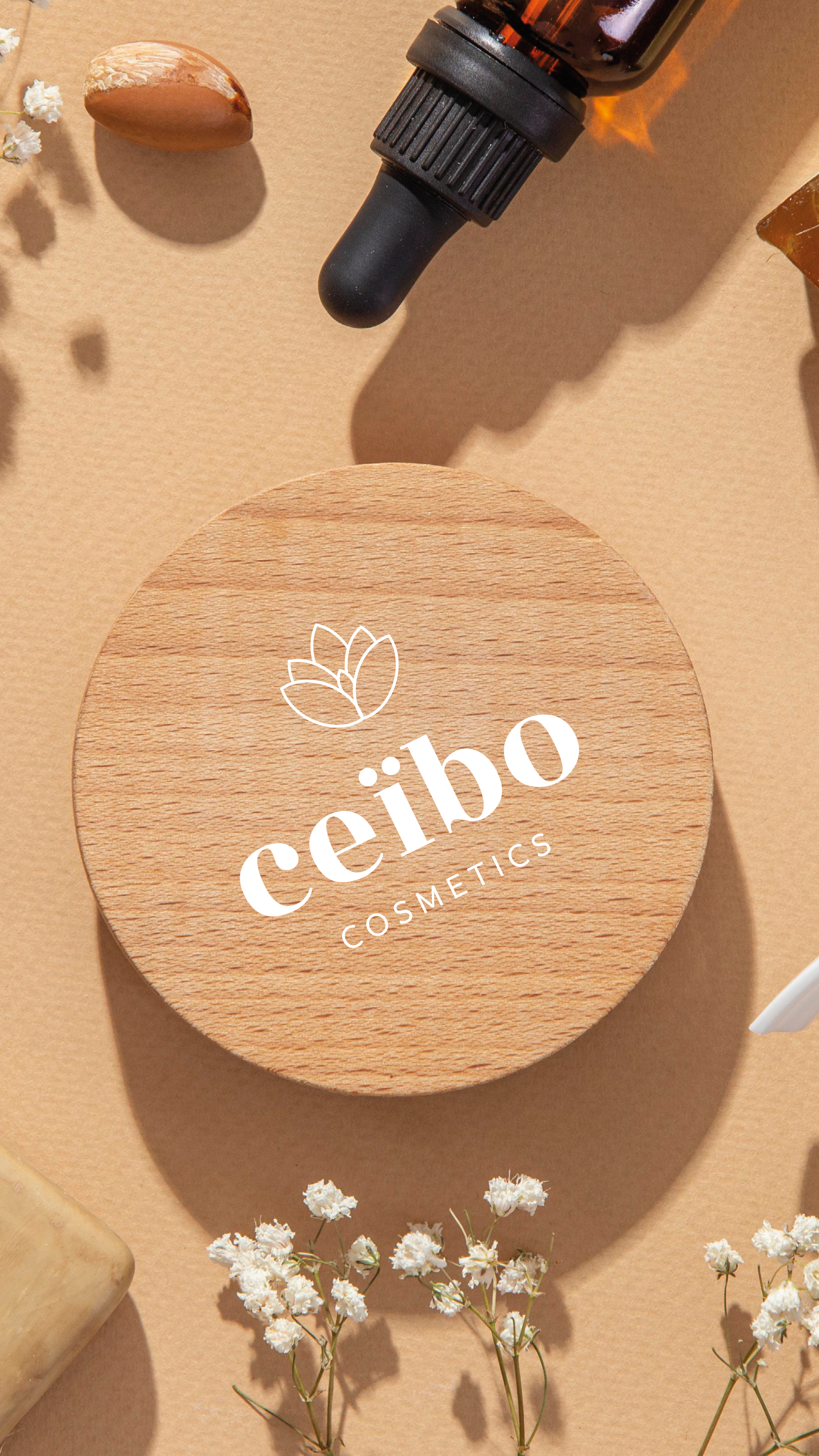 Un pot en bois avec le logo 'Ceibo Cosmetics', entouré d'éléments naturels et cosmétiques tels qu'une bouteille de goutte à goutte, des fleurs blanches, et un morceau de savon, sur un fond beige.