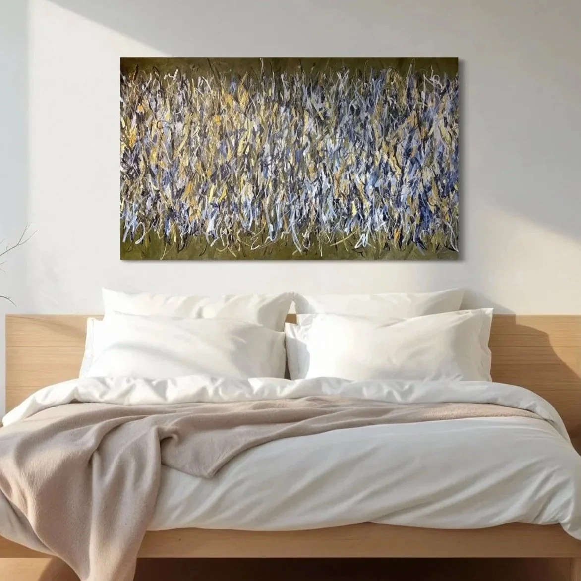 A bed with white pillows and a beige blanket in front of a white wall, with an abstract painting above the headboard.}