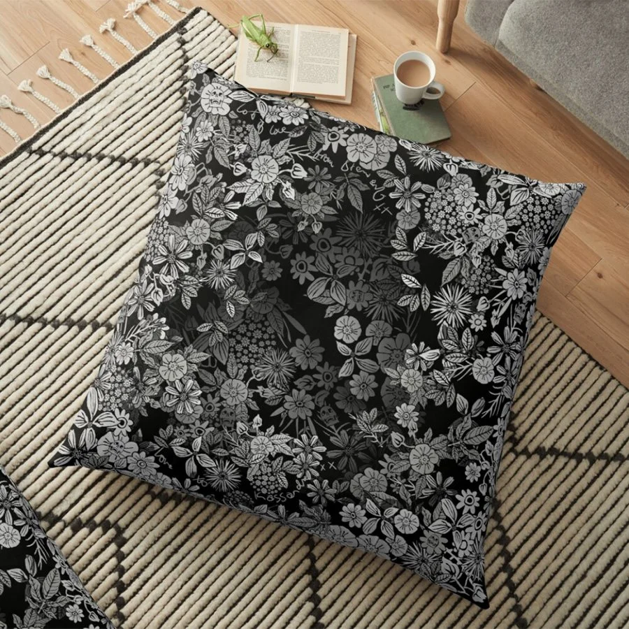 Czar Catstick Artwork via Pixels.com Fine Art America BFAHub Online BFAPrintsA black and white floral patterned pillow on a beige and black striped rug in a cozy living room corner with a book, green glasses, a mug of coffee, and a green book nearby.