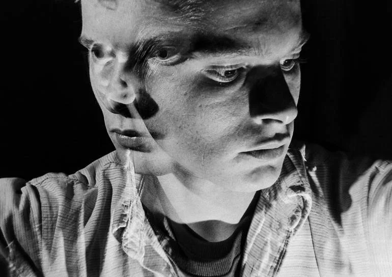 Self Portraits. Retro Collection. Black and white photo of a young man with a serious expression, looking down and to the side, with a layered, double exposure effect creating a ghostly appearance. Artist Czar Catstick BFA Hub Online British Bespoke 