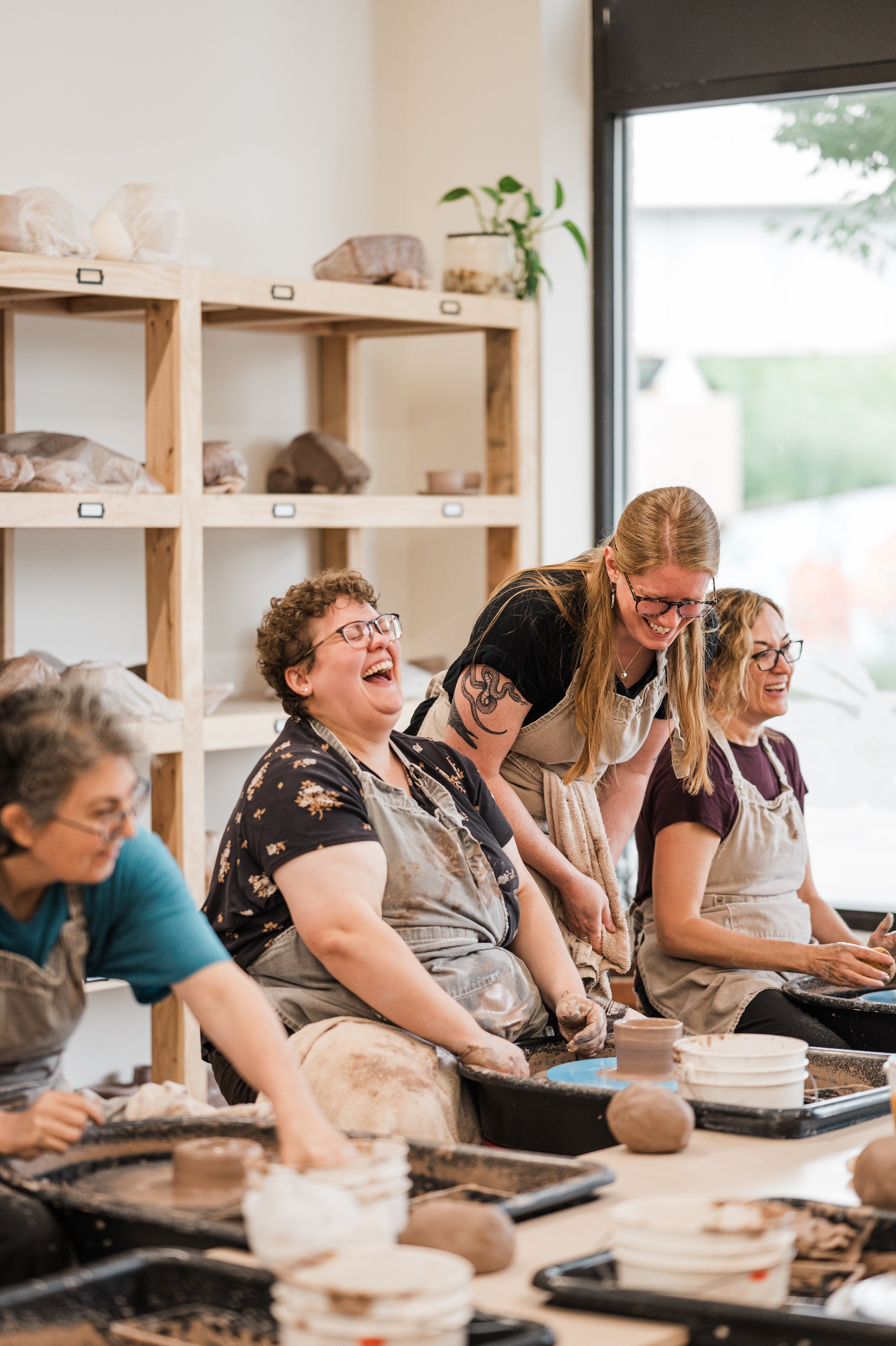 Three adults and their pottery wheel instructor laughing and having fun in a series course for beginners