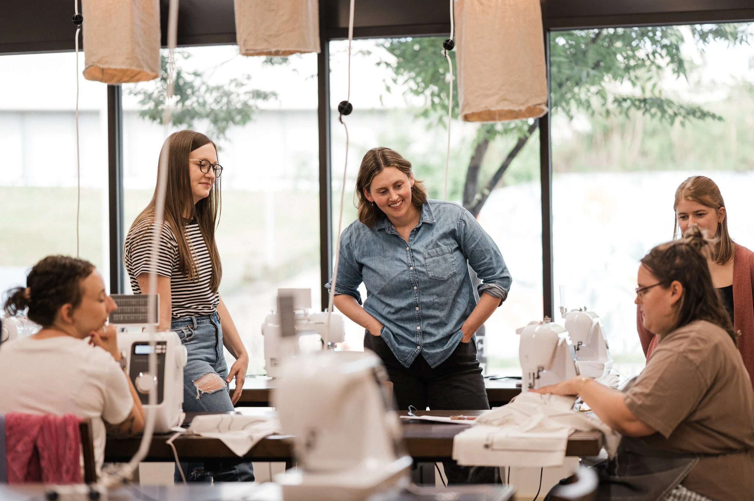 Adult beginners watching a sewing instructor teach how to sew on a machine
