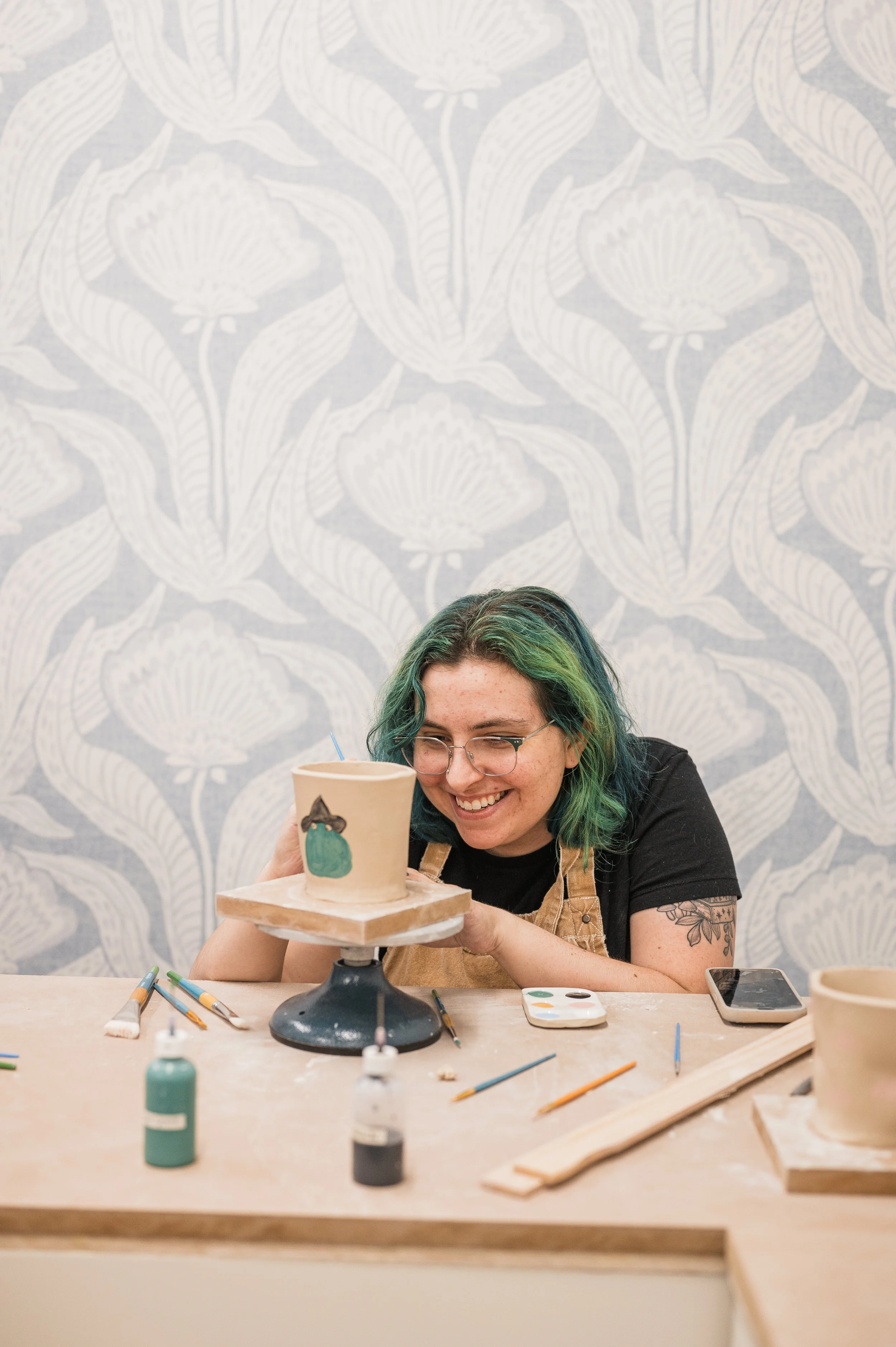 A young adult female smiling and glazing the cup she just made in a workshop experience