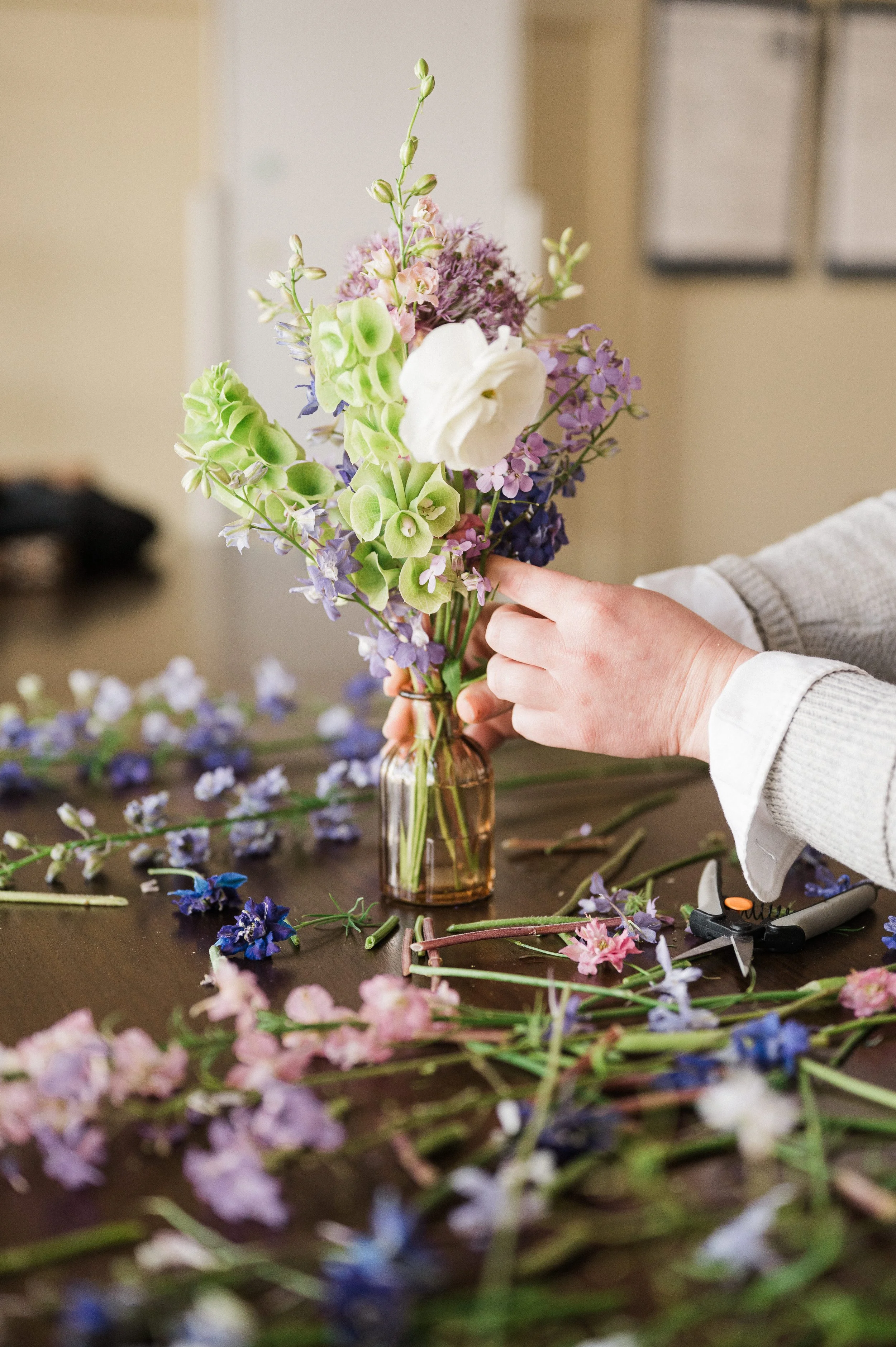 An adult arranging a floral bud vase in a private event workshop