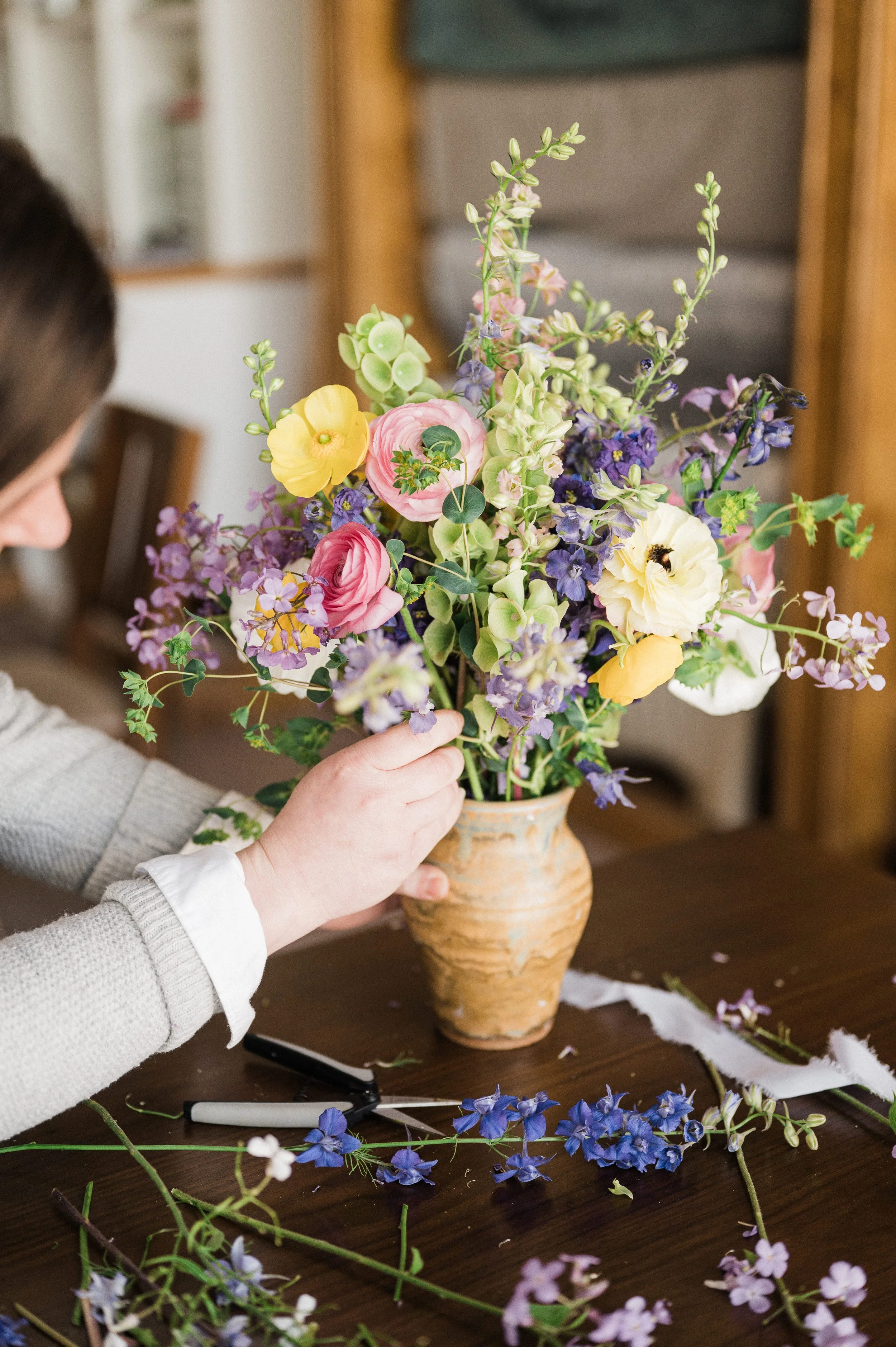 Adult creating a floral arrangement in a ceramic vase