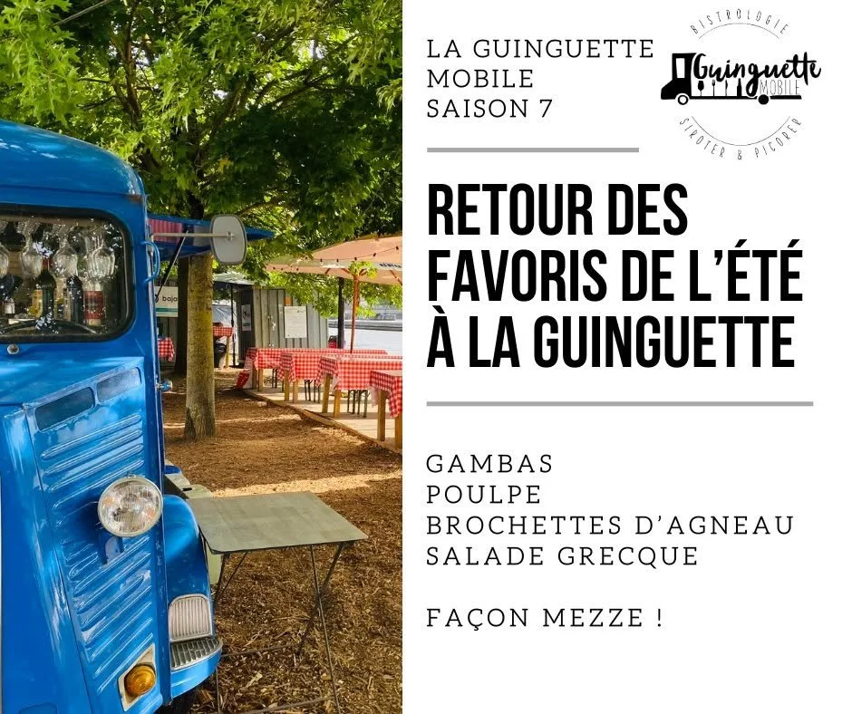Photo d'un food truck bleu garé dans un espace extérieur avec des tables à pique-nique avec nappes à carreaux rouges et blancs, ombragées par des parasols, entouré d'arbres.