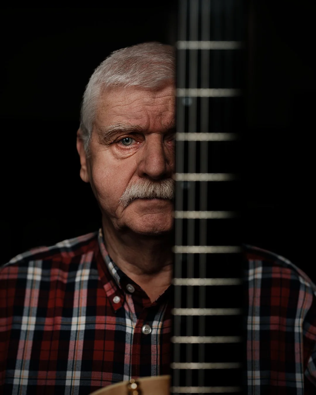 Portrait éditorial d’un homme à la guitare, éclairage sculpté et ambiance sombre mettant en valeur les textures et l’intensité du regard.