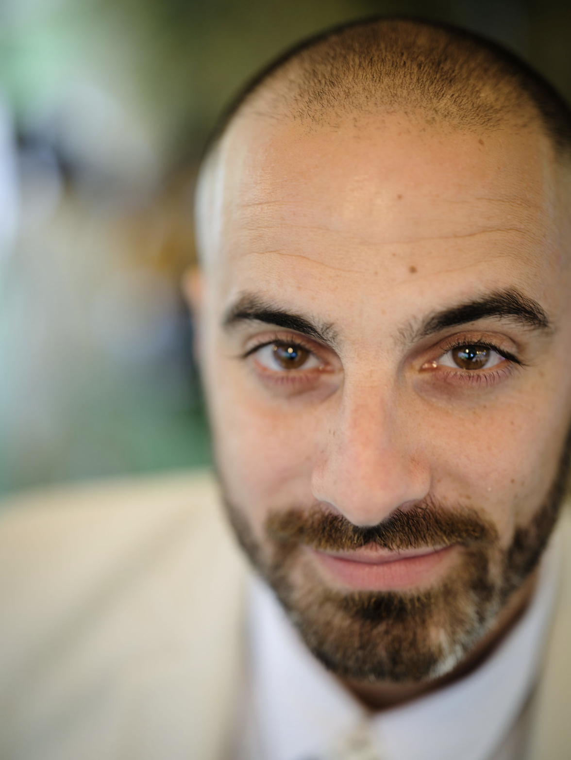 Un homme avec une barbe, yeux marron, et une tête rasée, regardant légèrement vers le haut.