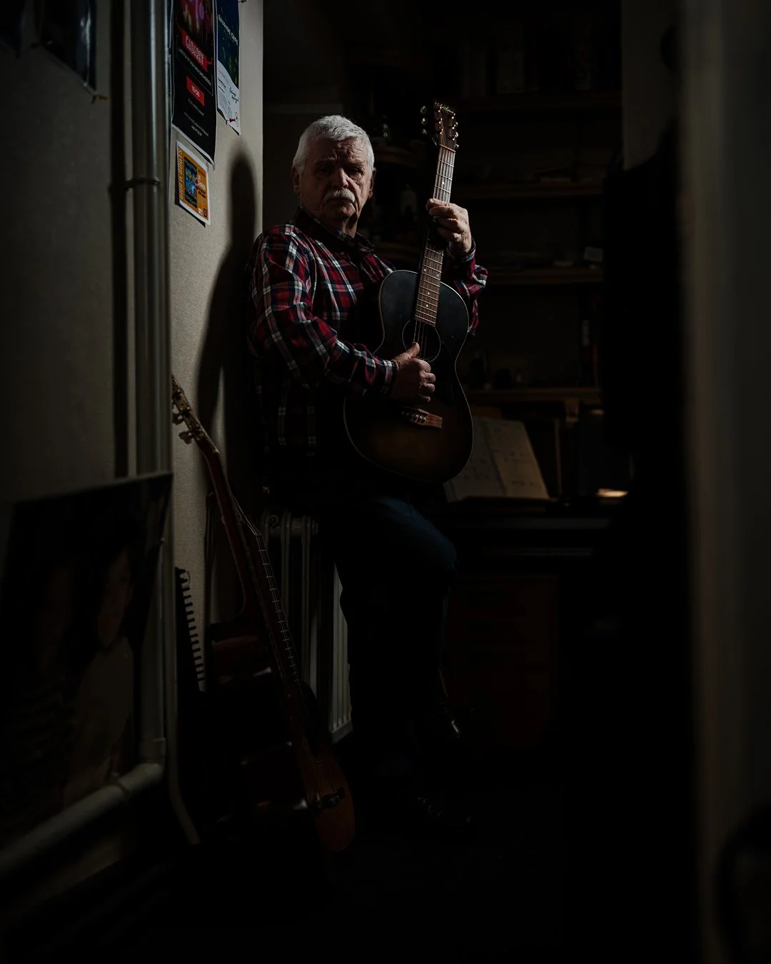 Portrait éditorial d’un homme à la guitare, éclairage sculpté et ambiance sombre mettant en valeur les textures et l’intensité du regard.
