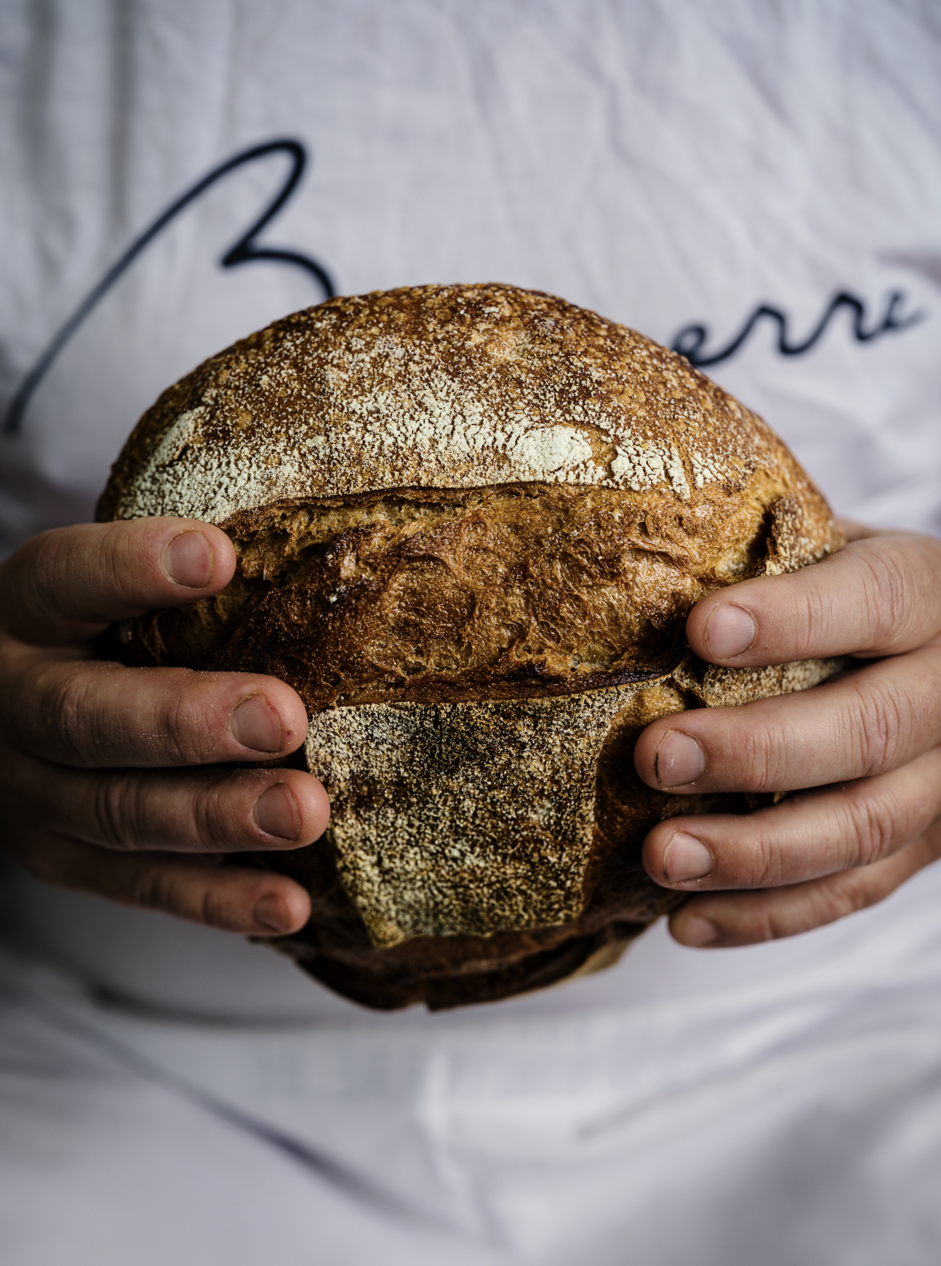 Personnes tenant un pain artisanal rond avec une croûte dorée et une texture glutenuse.
