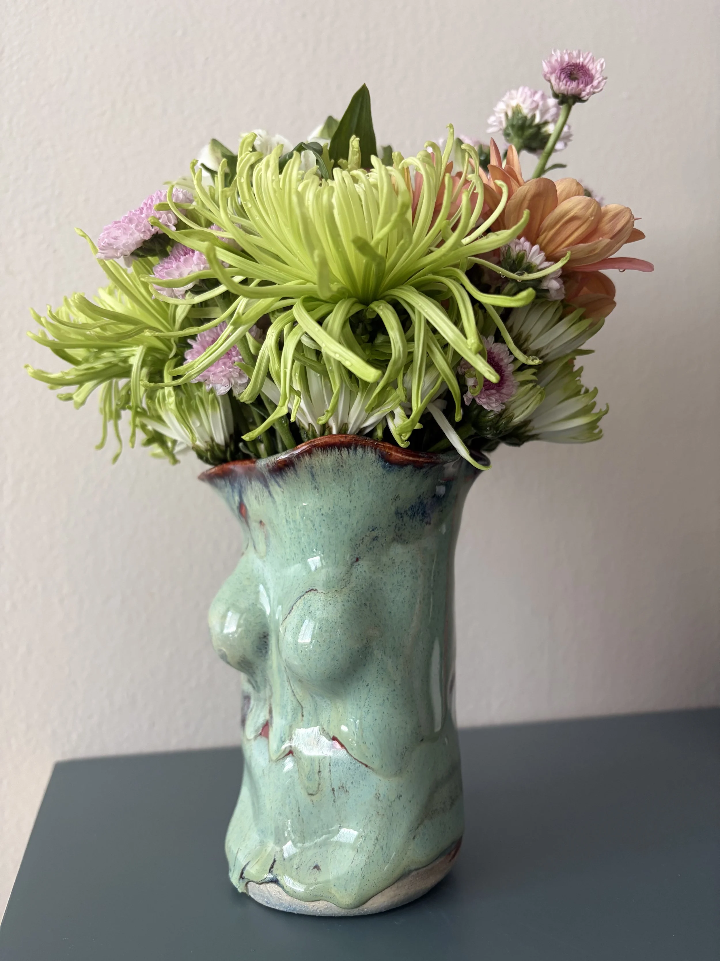 Side view of a small sculpted ceramic body vase with a ruffled floral opening