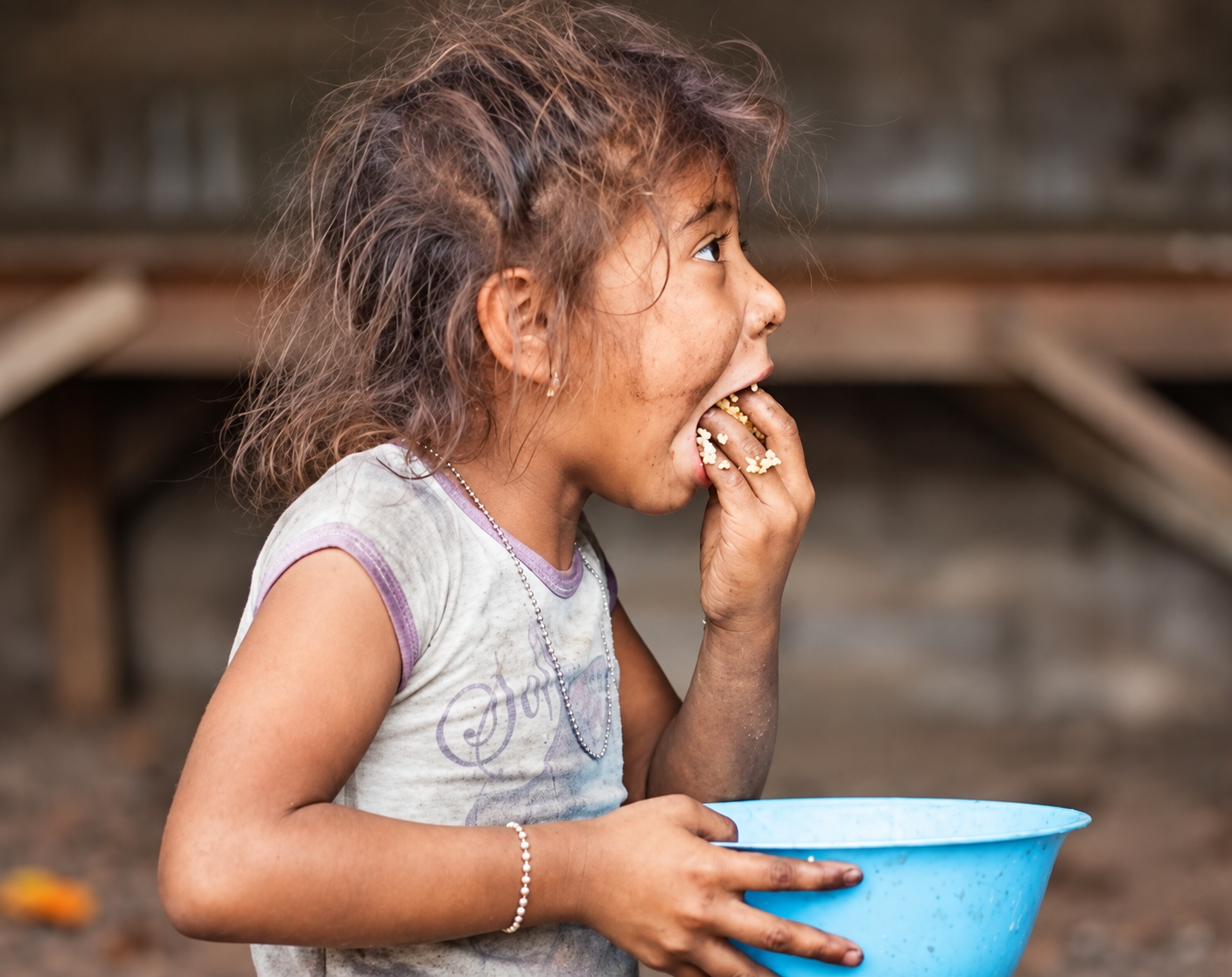 A child eating while holding a blue bowl.