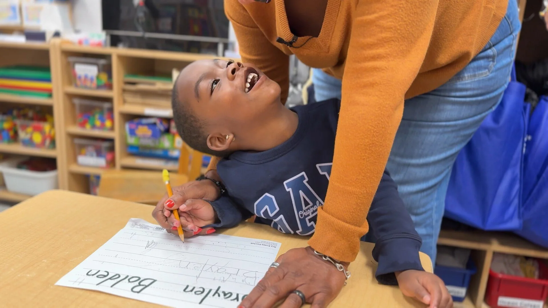 Still image from the film "Raising Superheroes" showing a teacher assisting their child student
