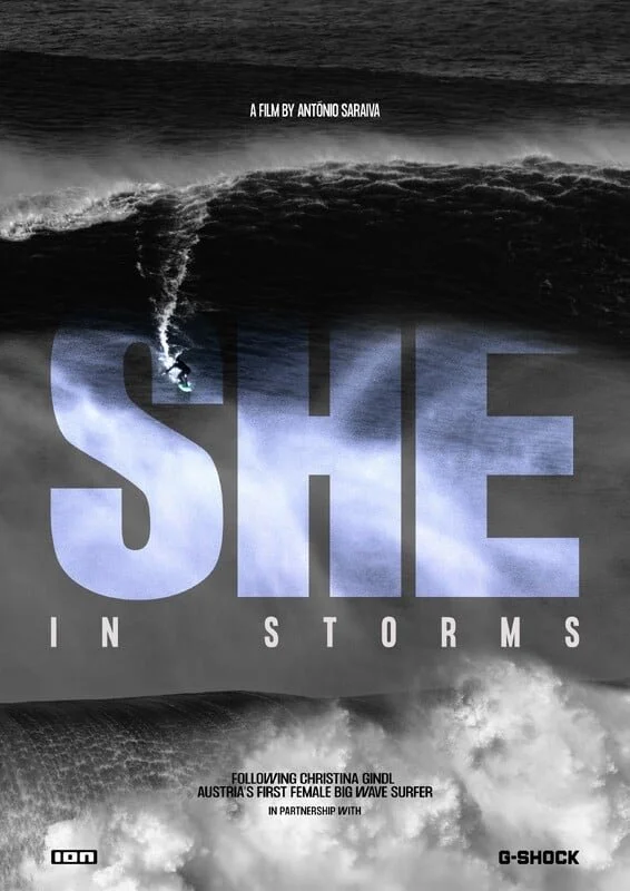 Black and white image showing a large ocean wave with a surfer riding inside its curl. Overlaid text includes the film title 'SHE IN STORMS' and details about the film by Antonio Saravia and Christina Gindl, about Austria's first female big wave surfer, in partnership with G-Shock.